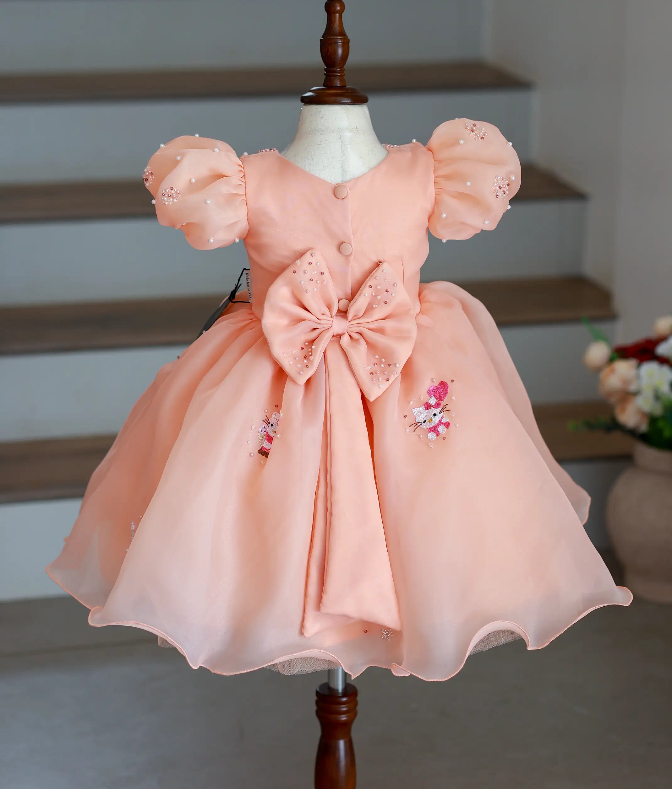 Back view of the peach Hello Kitty frock highlighting the large handworked decorative bow and button closure