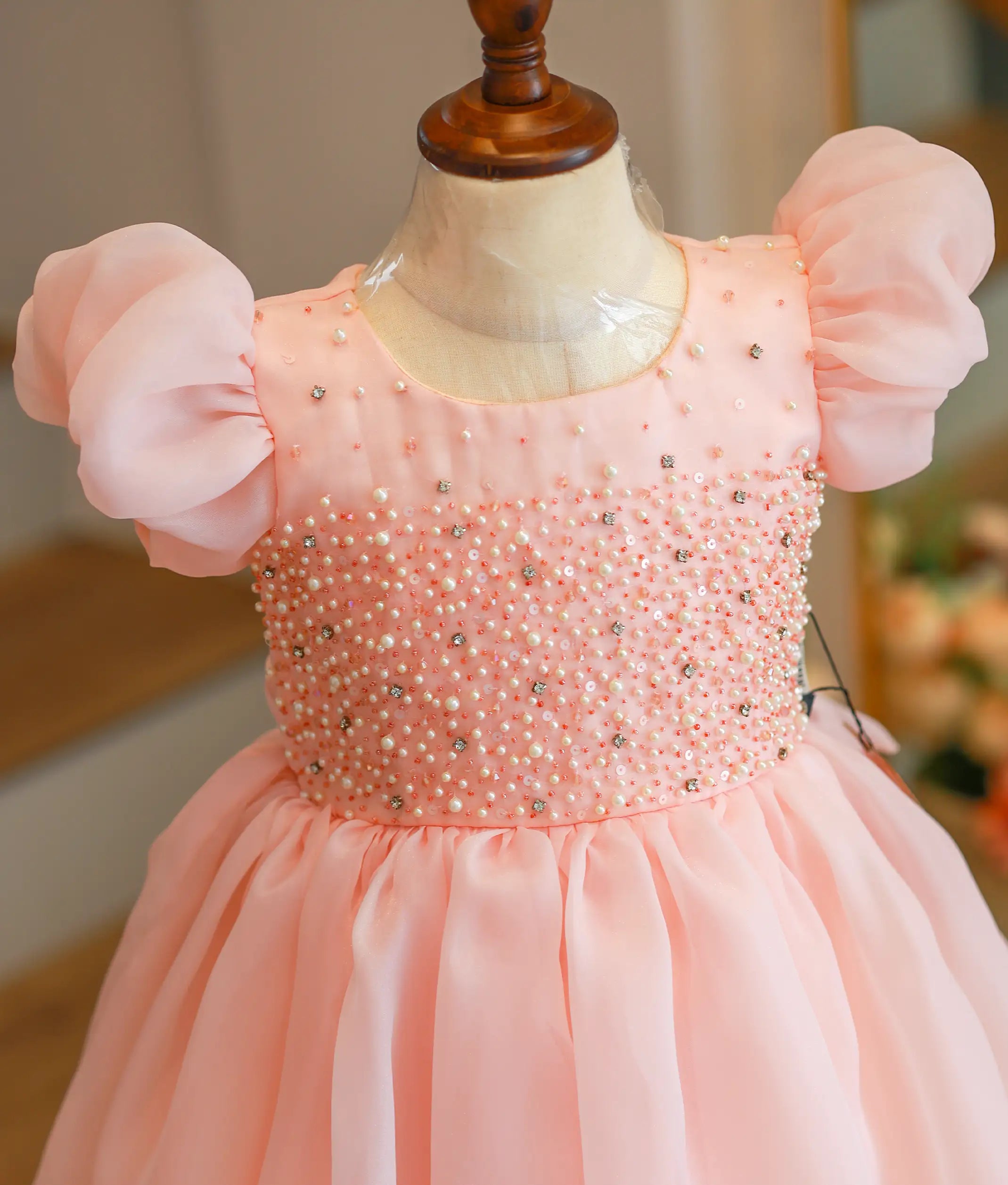 Close-up of the peach organza frock showing the detailed handwork on the yoke and the elegant puff sleeves