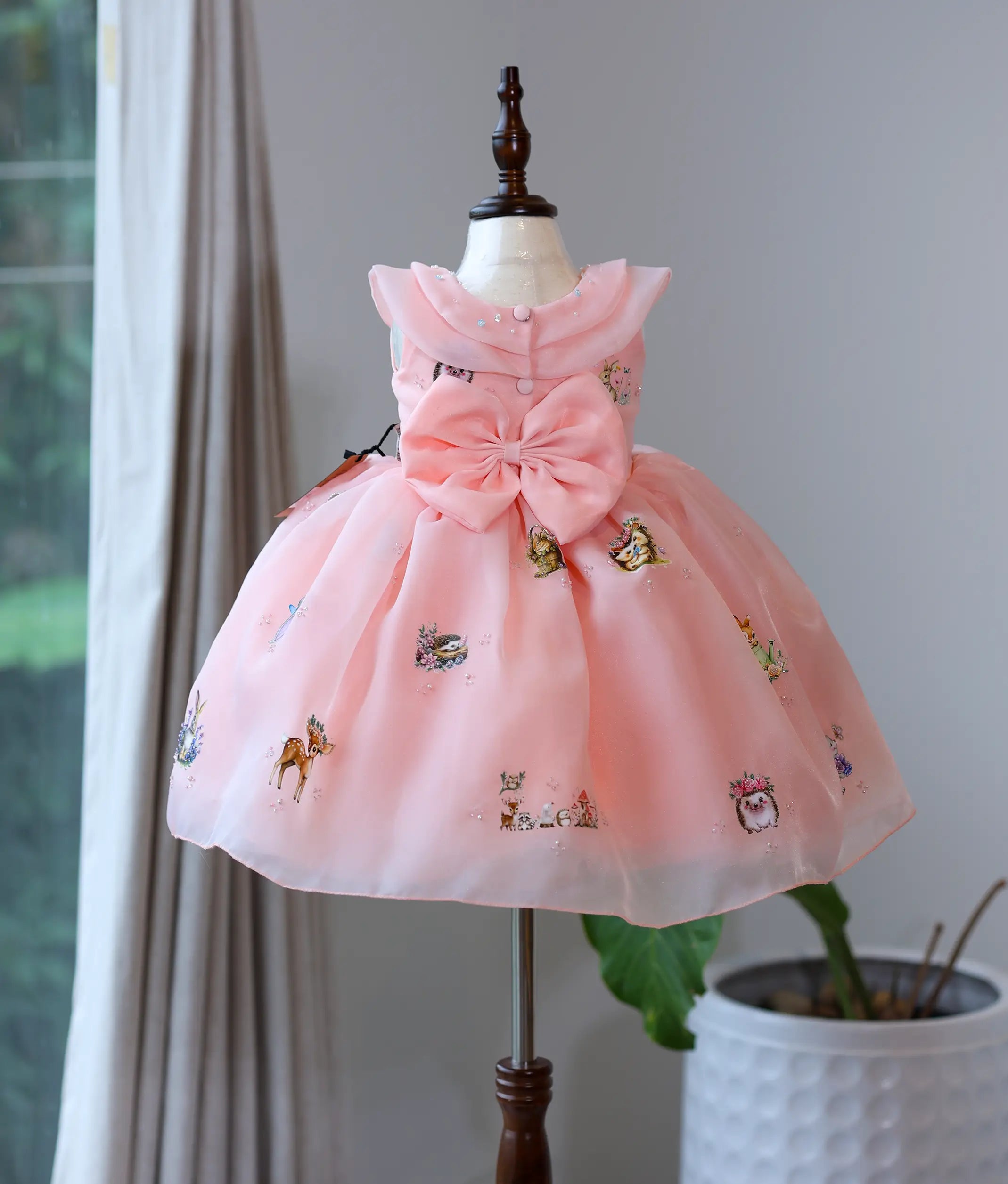 Back view of peach pink organza frock showing round neck, show buttons, and statement bow.