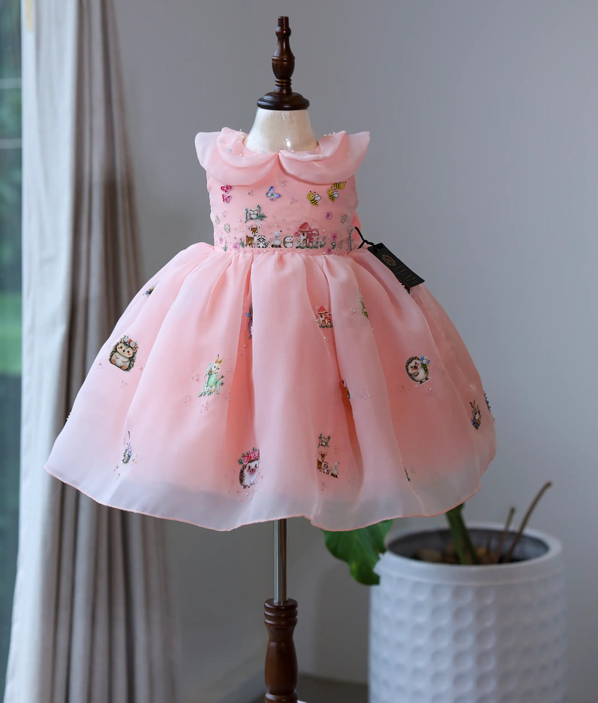 Peach pink plain organza handworked woodland theme frock for baby girl on a mannequin.