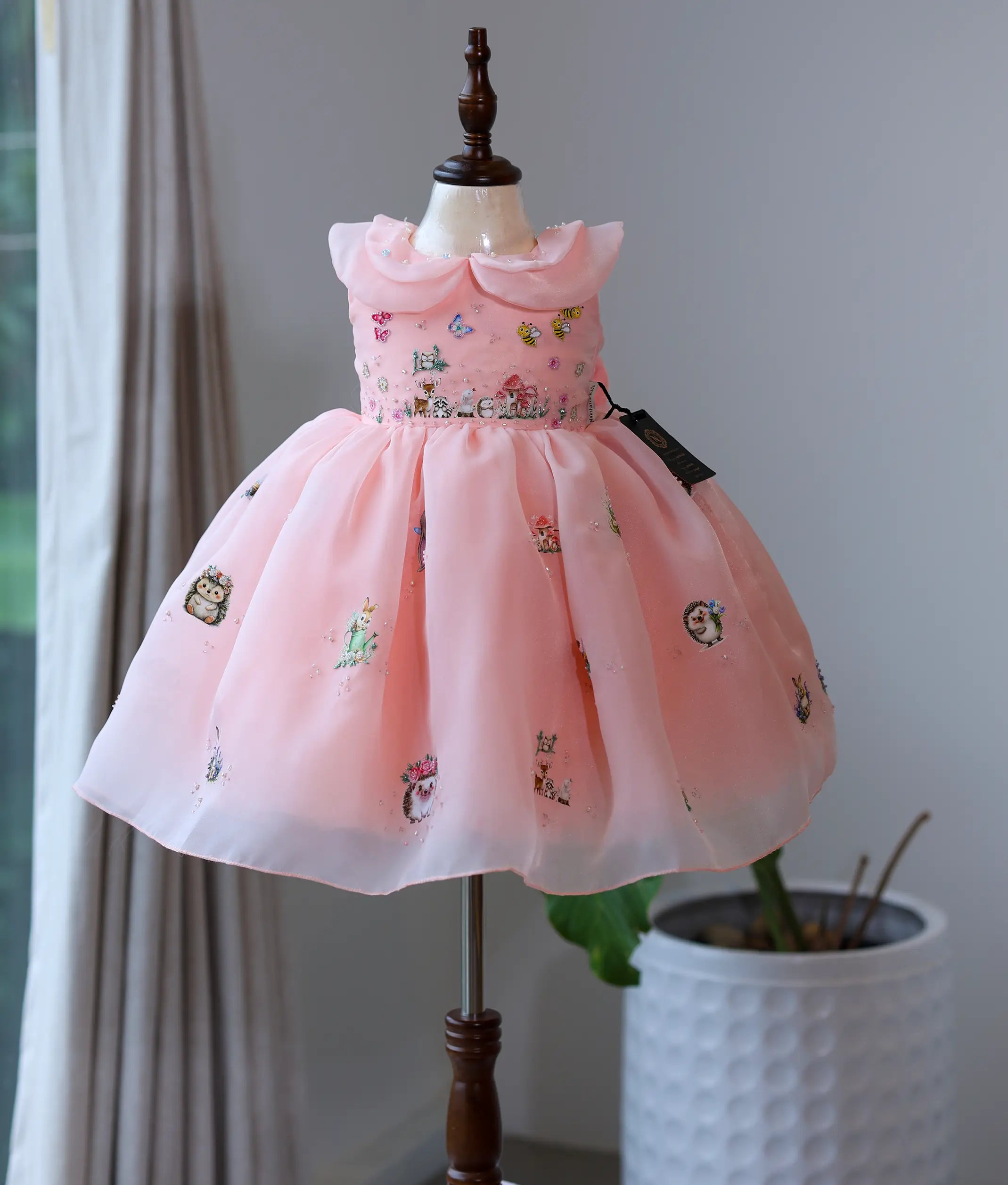 Peach pink plain organza handworked woodland theme frock for baby girl on a mannequin.