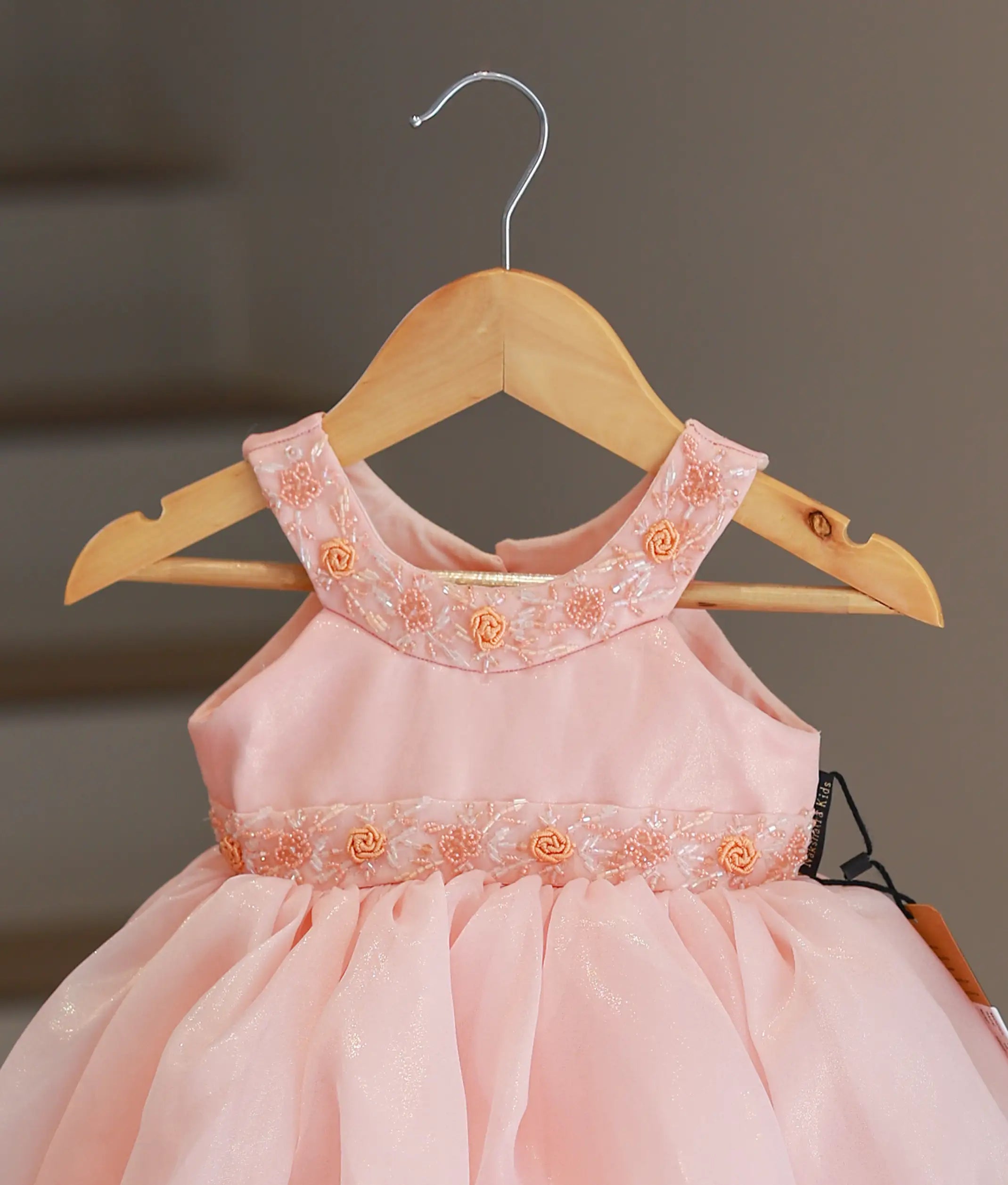 Close-up of the peach frock showing the hand-embroidered floral collar and the belt-style handwork on the yoke.
