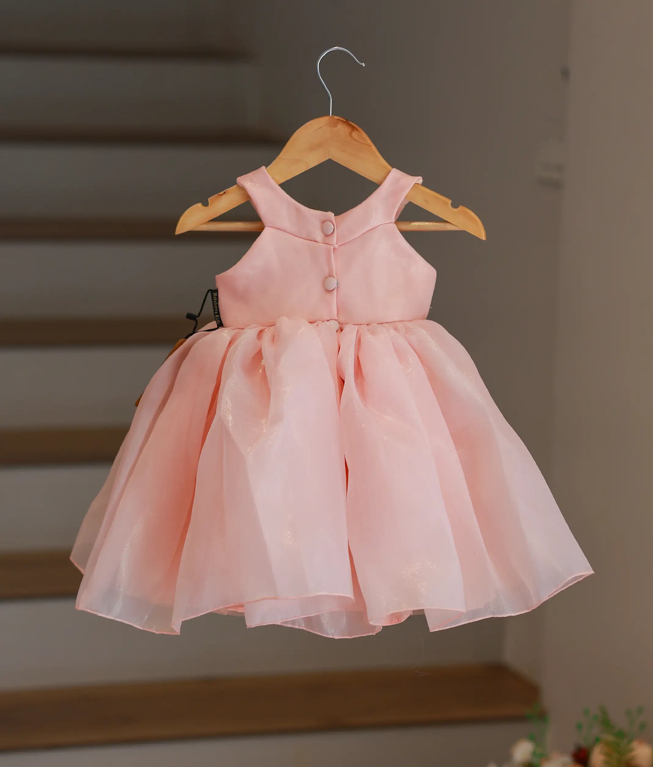 Back view of the peach shimmer organza birthday frock highlighting the halter design and button closures.