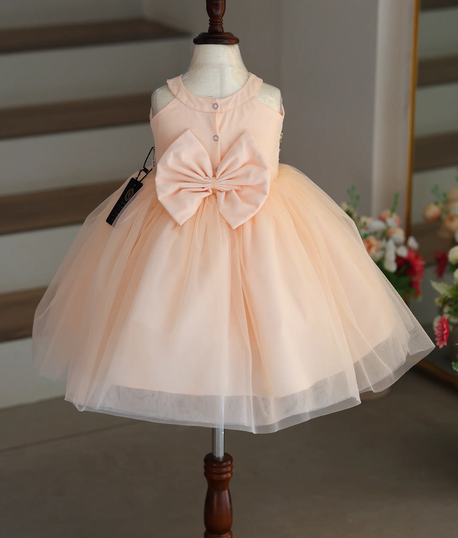 Back view of the peach halter neck frock showing the statement bow and button fastening.