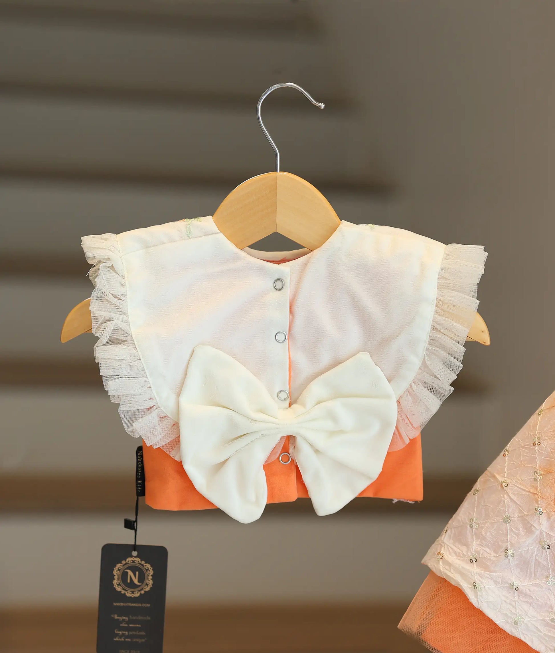 Back view of the peach and off-white set showing the pleated net neck, button closure, and decorative bow