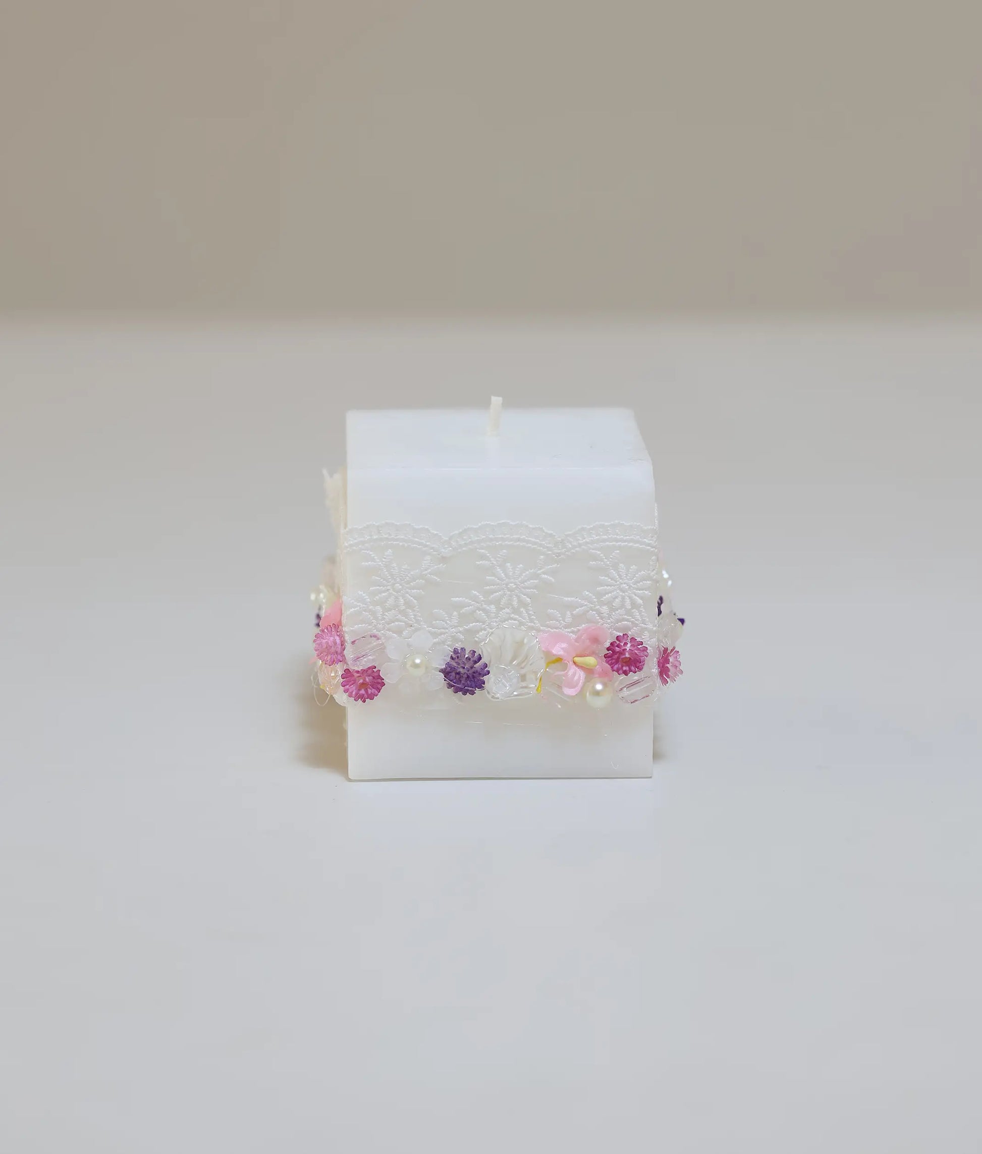 Decorative baptism candle featuring pink and purple silk flowers, white lace ruffles, and pearl accents
