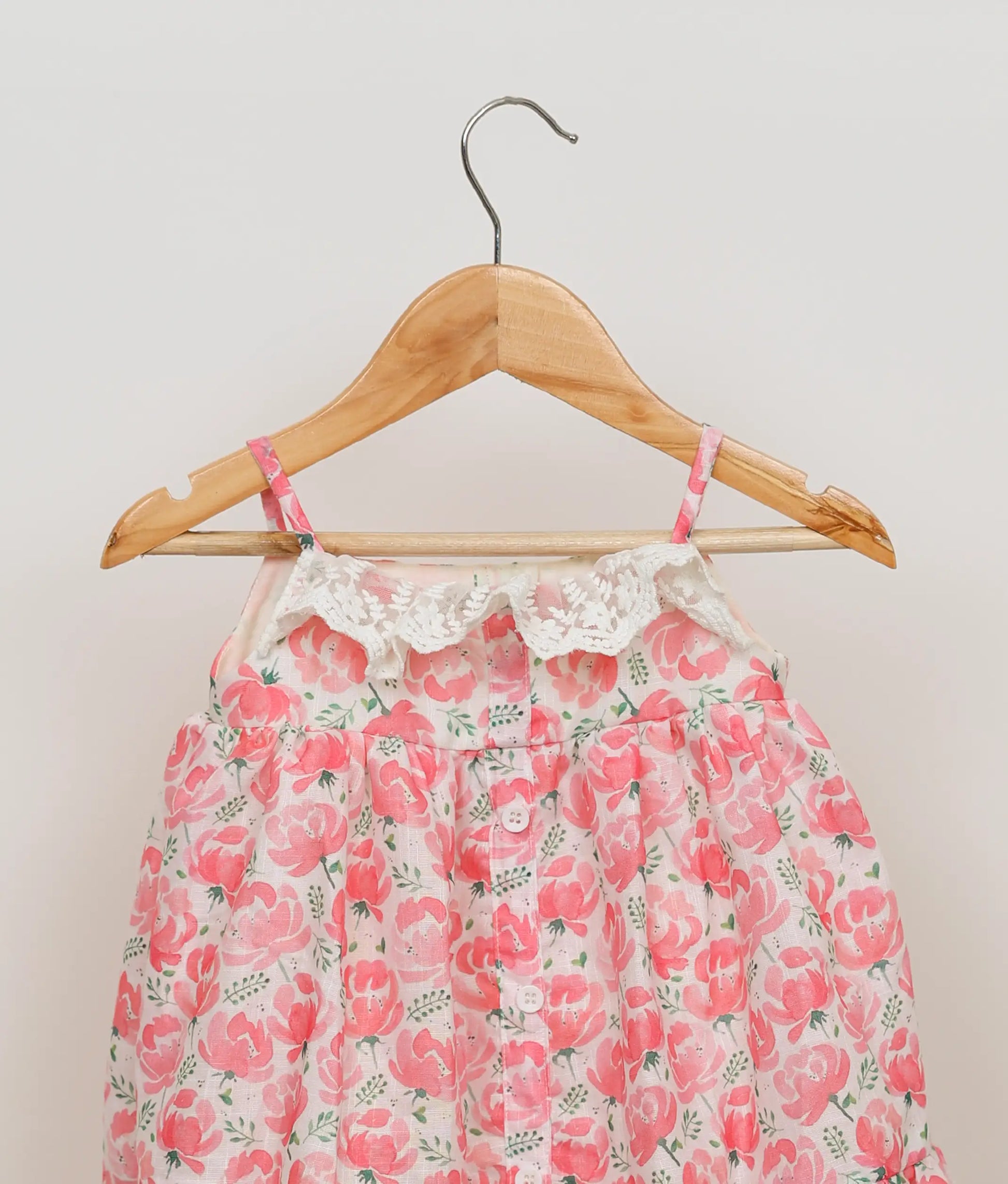 Close view of pink floral-printed cotton christmas frock against plain background.