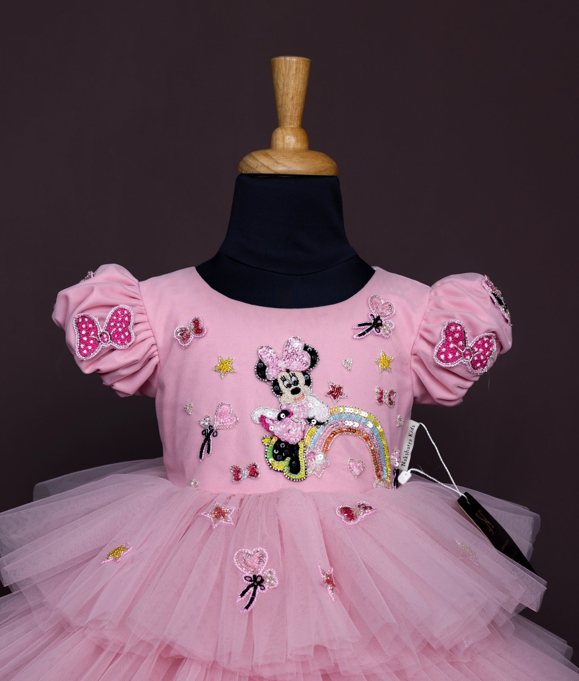 Close view of a pink baby girl dress with puff sleeves, Minnie Mouse sequin work, and a layered net tulle skirt.