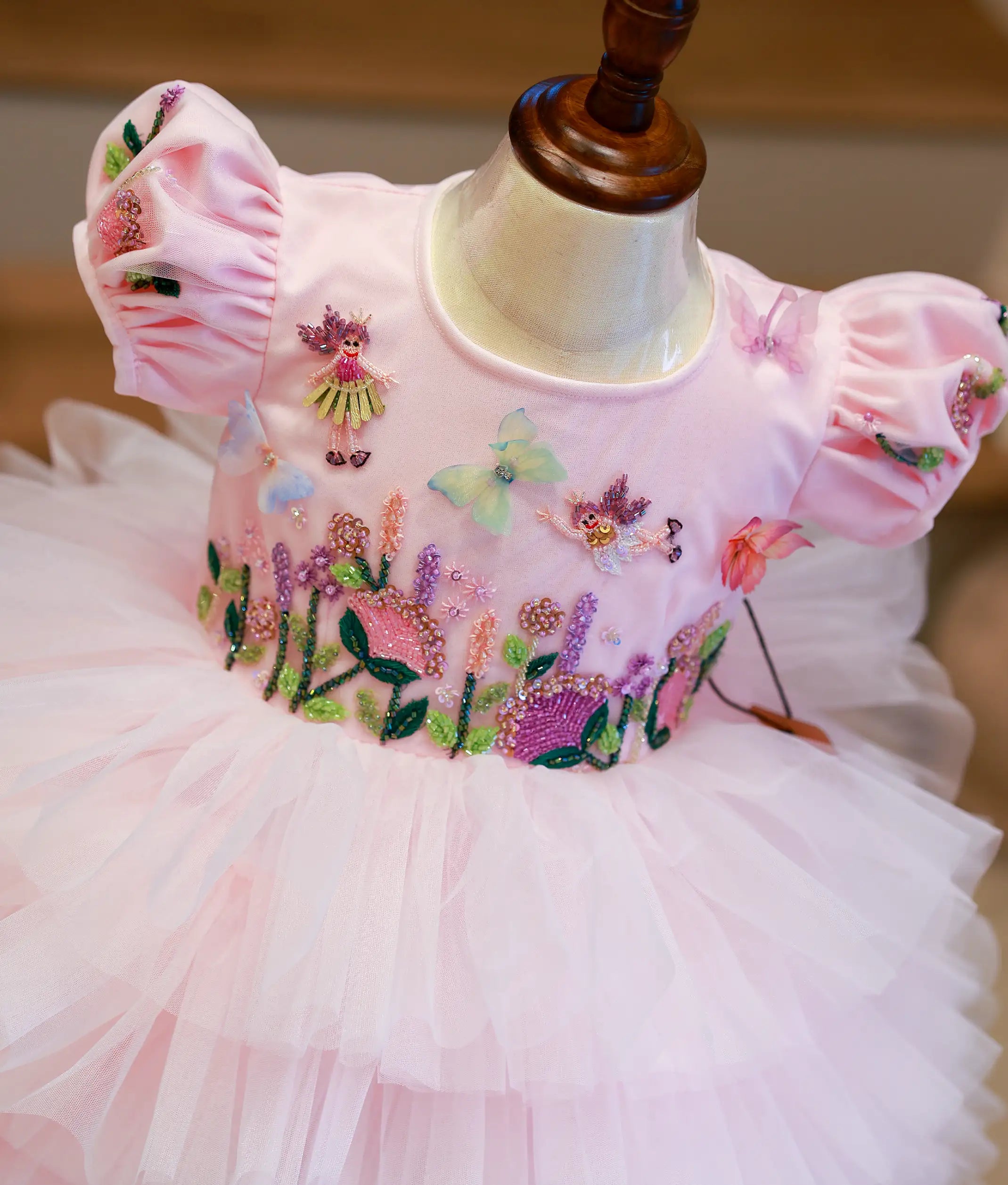 Close-up of the intricate princess and butterfly handwork with beads and sequins on the pastel pink bodice.