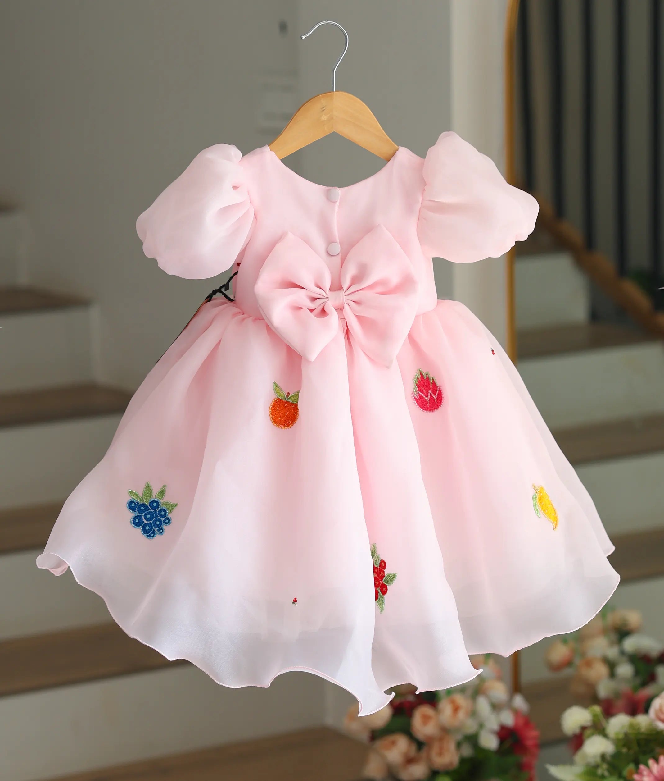 Back view of the pastel pink organza frock showing the large bow and button closure.