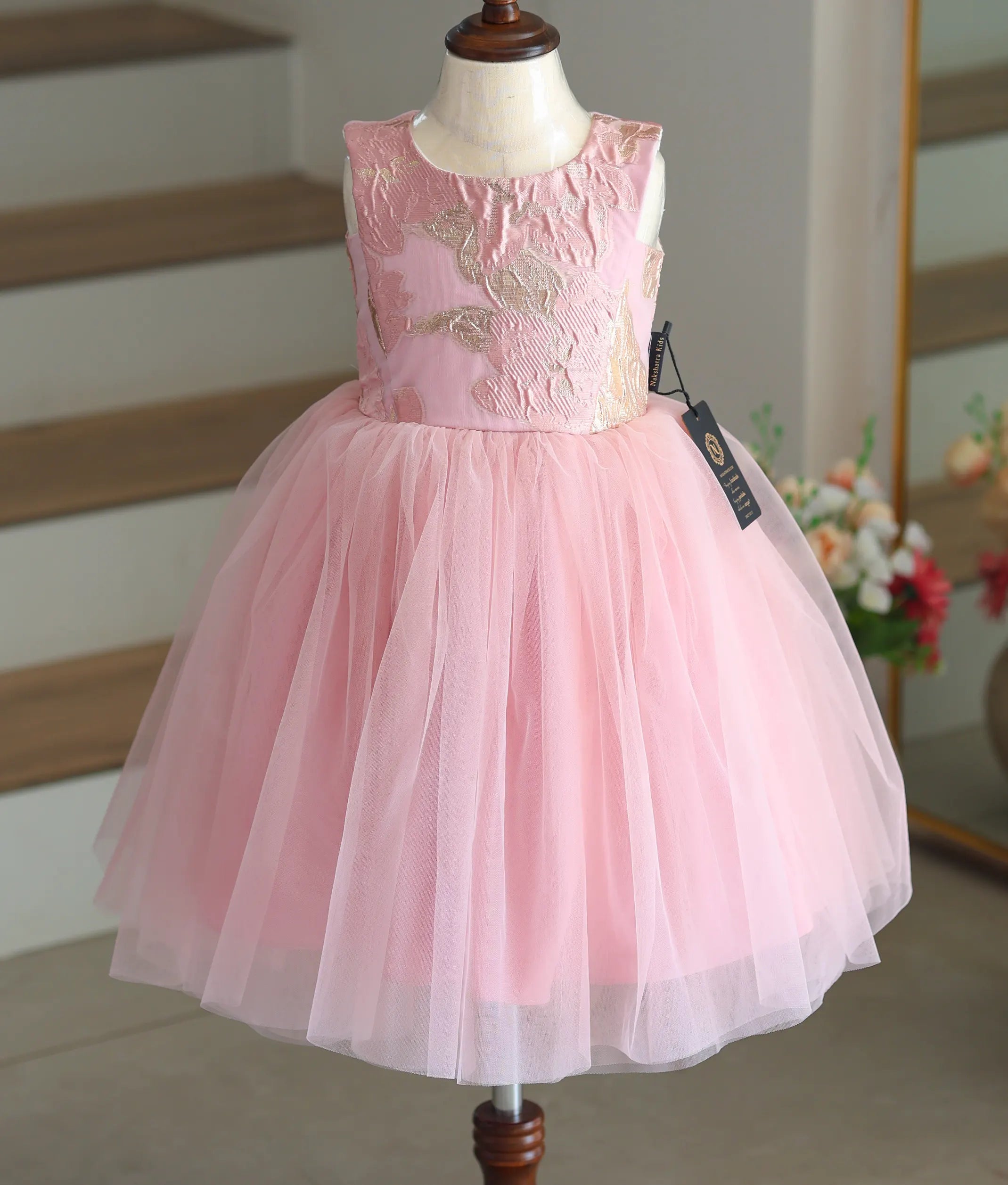 Front view of a pink tulle net frock with a golden leaf-pattern organza top.