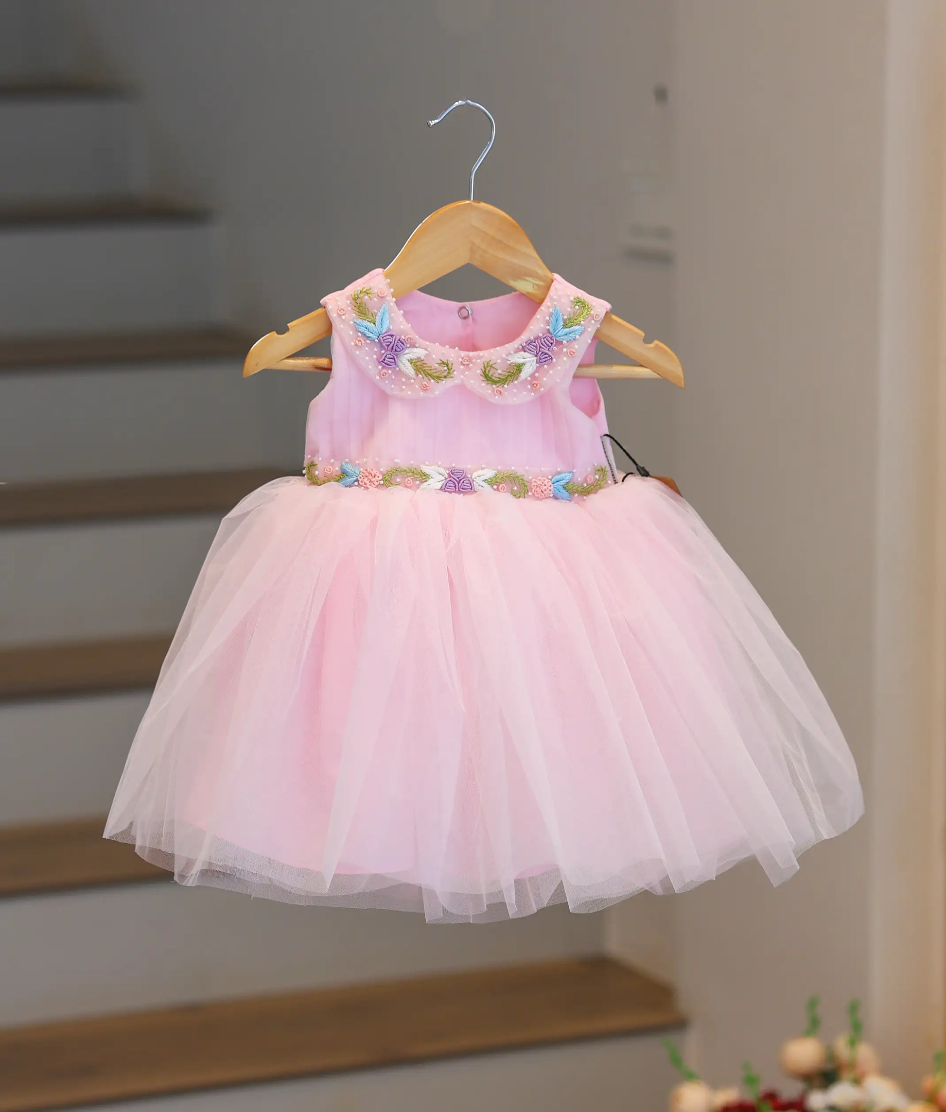 Front view of a pink pleated bodice frock featuring pearl handwork and a floral belt.