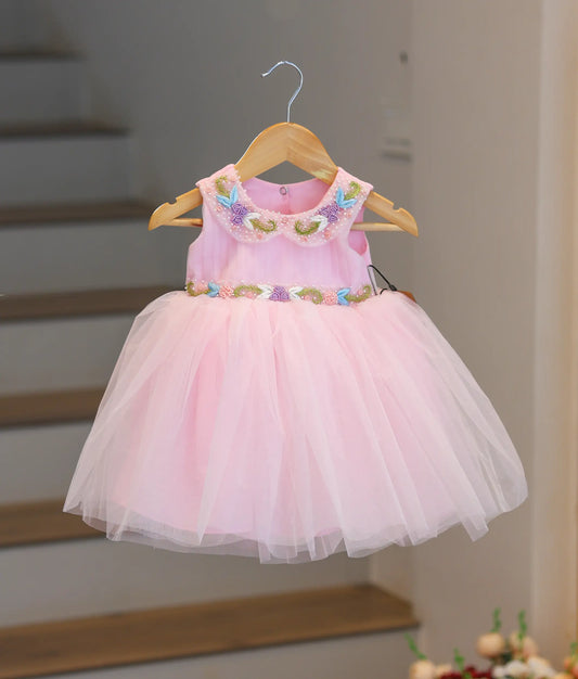 Front view of a pink pleated bodice frock featuring pearl handwork and a floral belt.