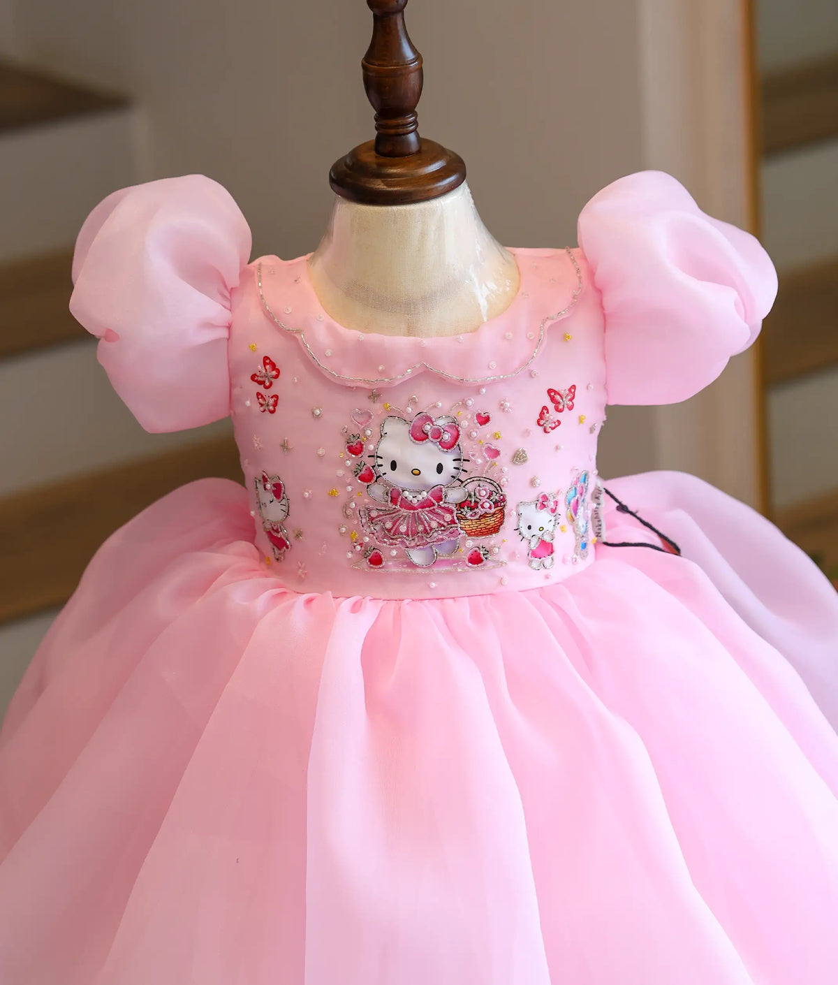 Close-up view of a pink frock showing Hello Kitty beadwork, sequin embroidery, and puff sleeves.