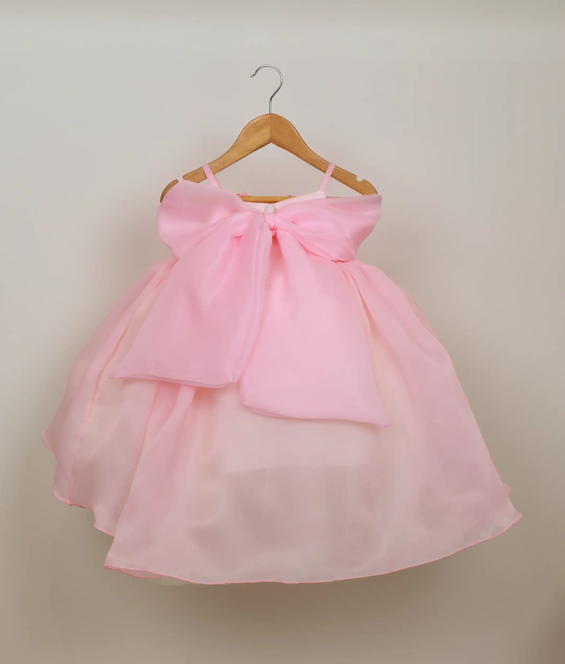 Back view of the pink high-low frock highlighting the decorative bow, show button, and adjustable waist tie