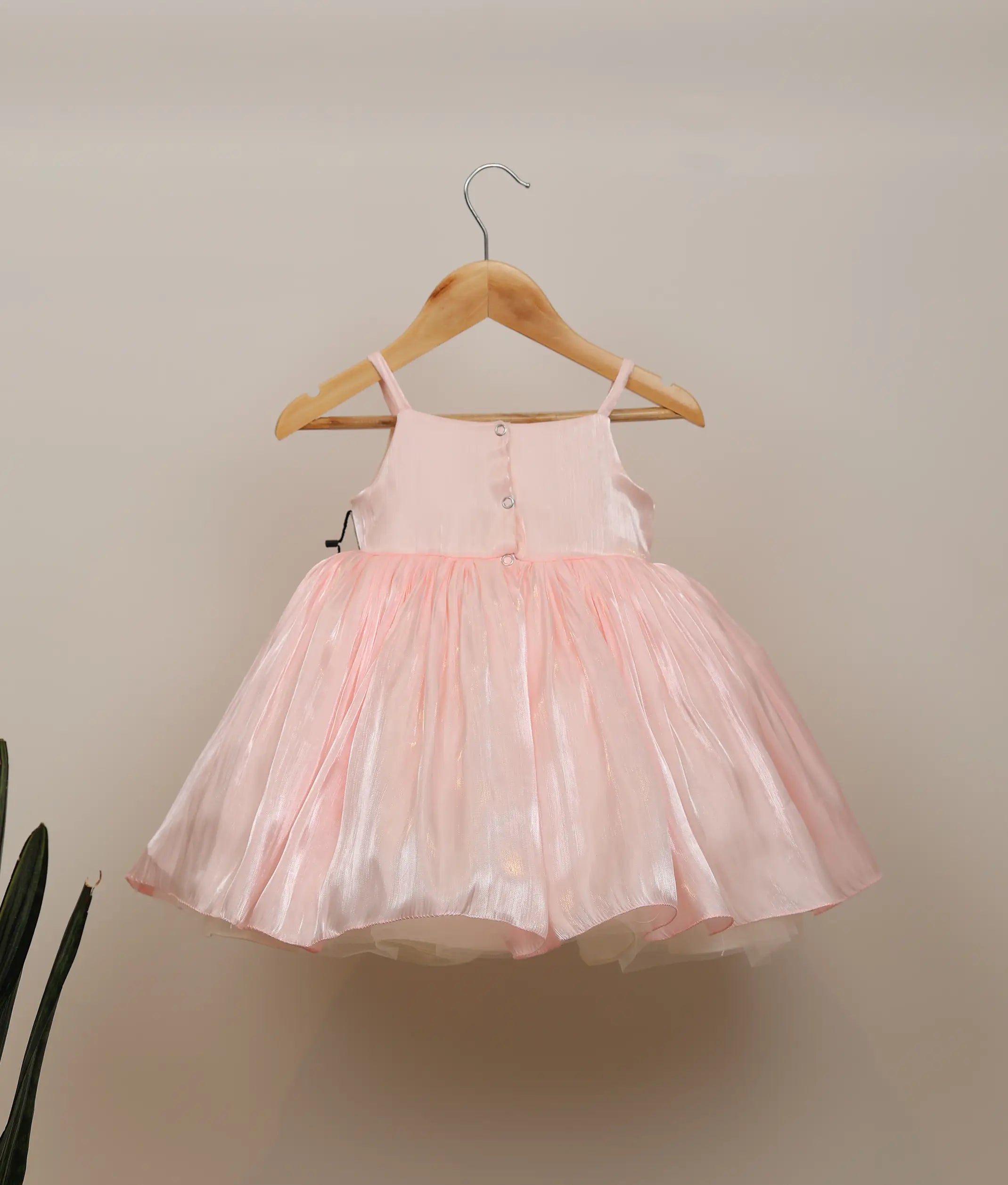Back view of pink laser organza frock showing the square neck design with button closure and the layered flared skirt