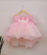 Front view of a pink organza high-low birthday frock for baby girls with floral handwork and a flared skirt