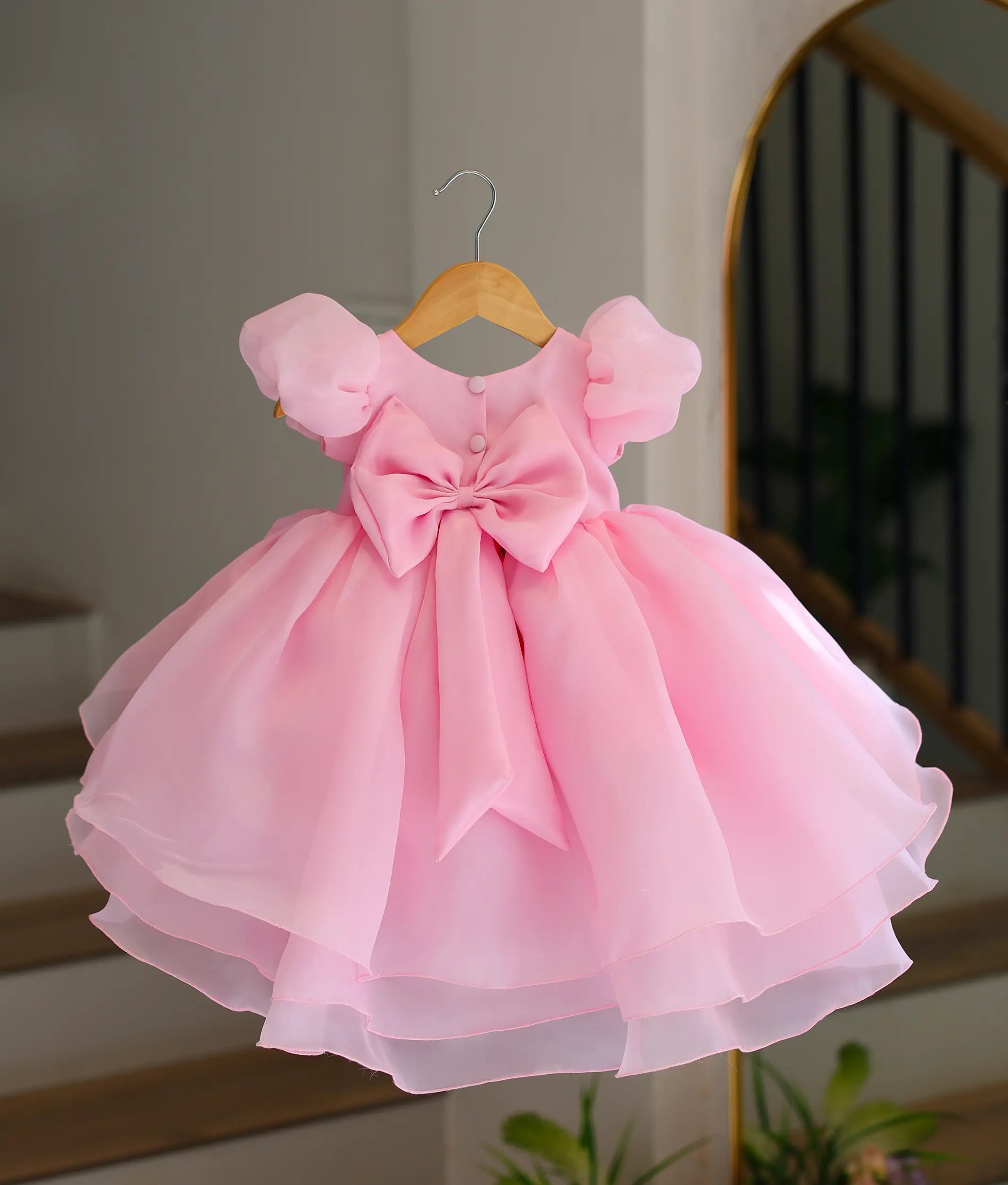 Back view of pink high-low frock for baby girl with button closure and bow detail