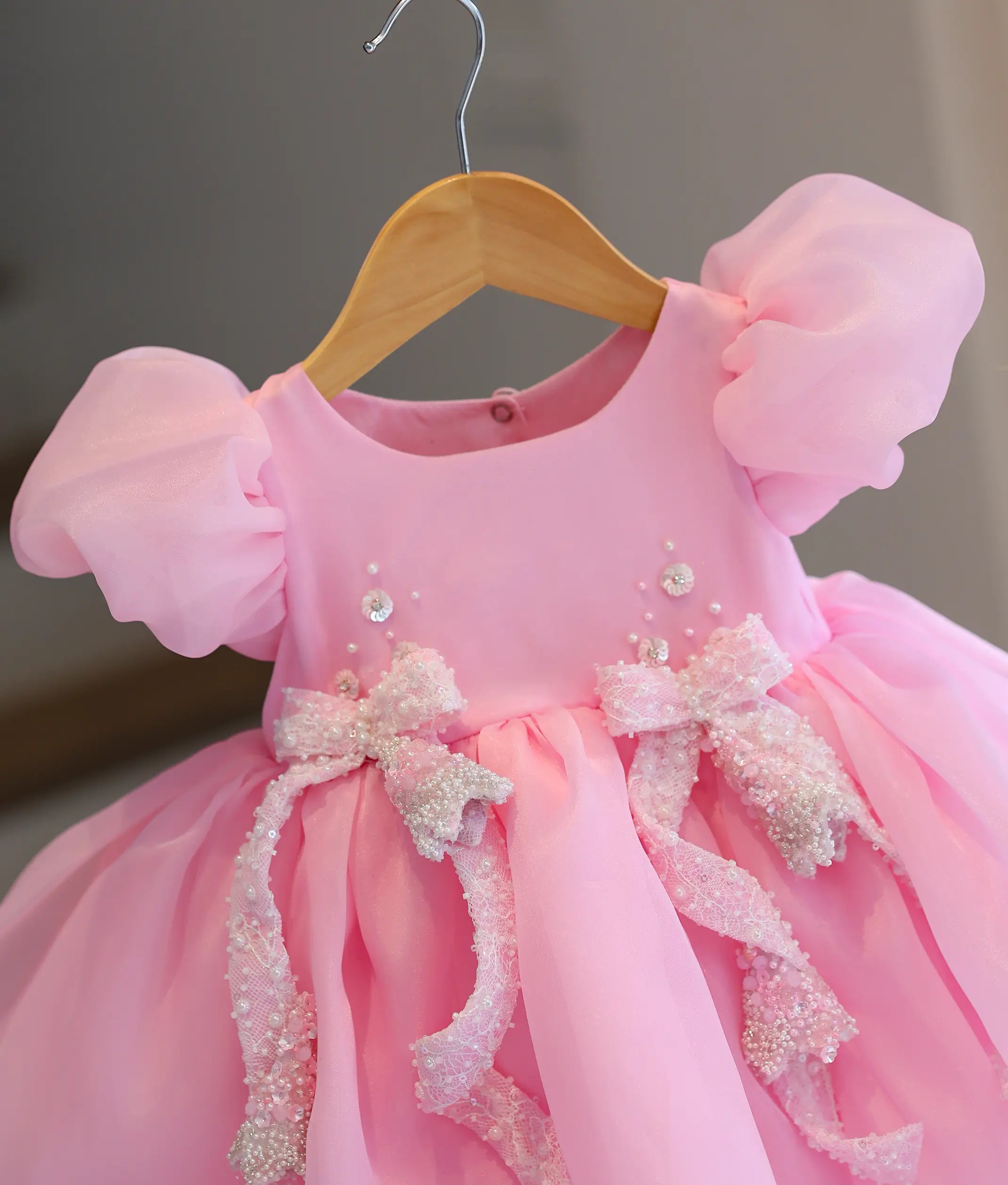 Close-up of sequin and bead floral handwork with bows on baby girl's pink birthday frock