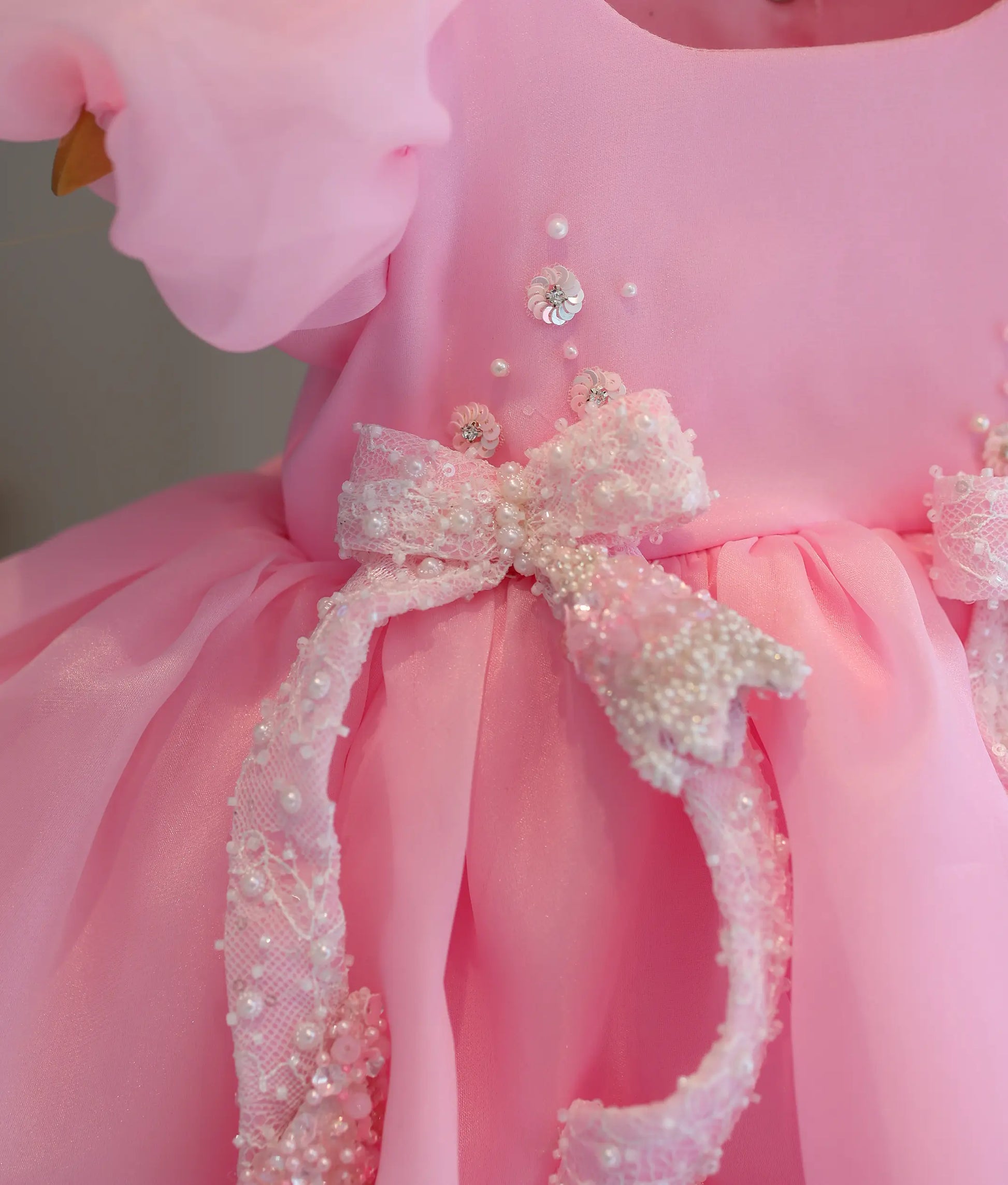 Close-up of sequin and bead floral handwork with bows on baby girl's pink birthday frock