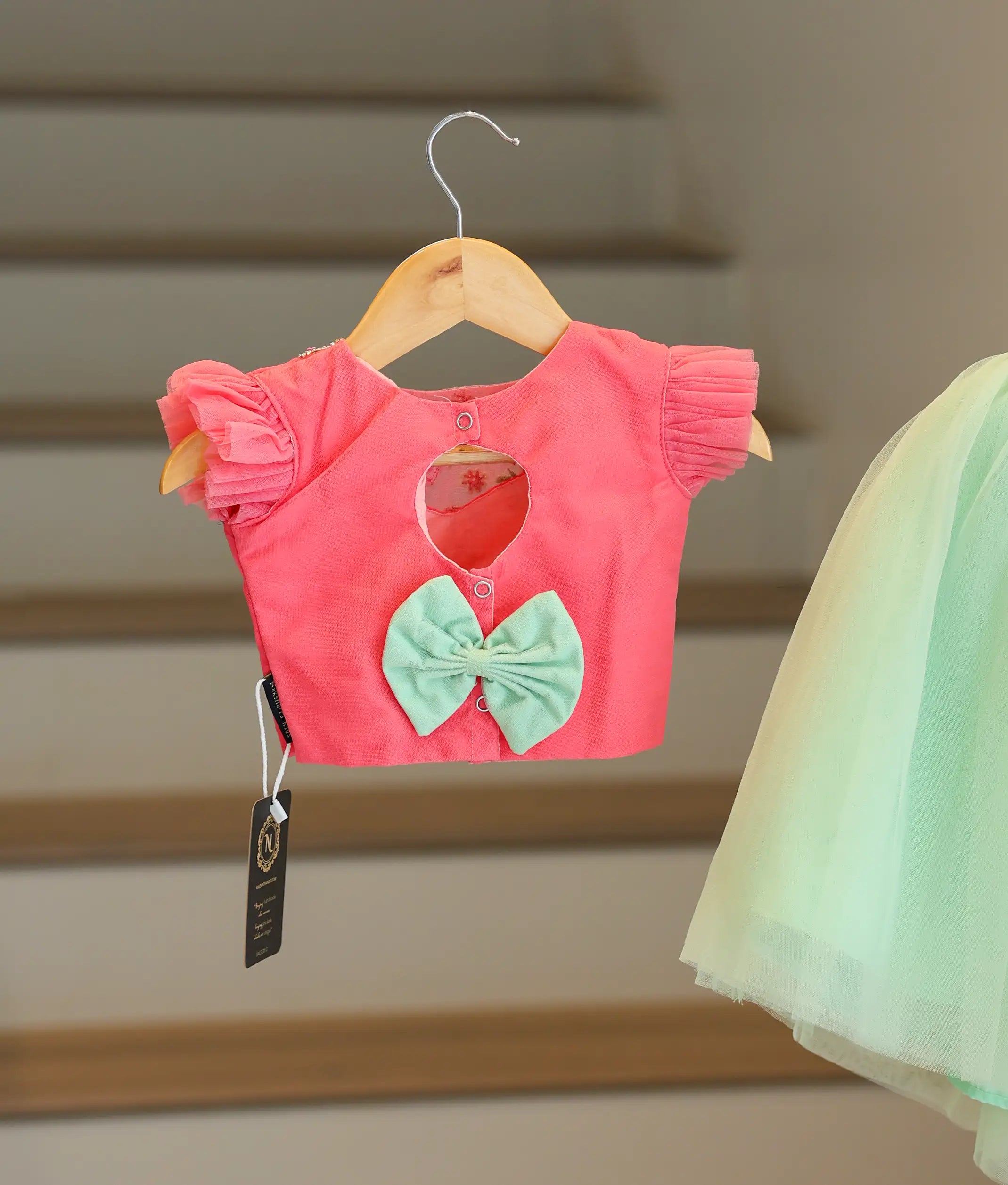 Back view of the pink and peach set showing the keyhole opening, button closure, and decorative bow