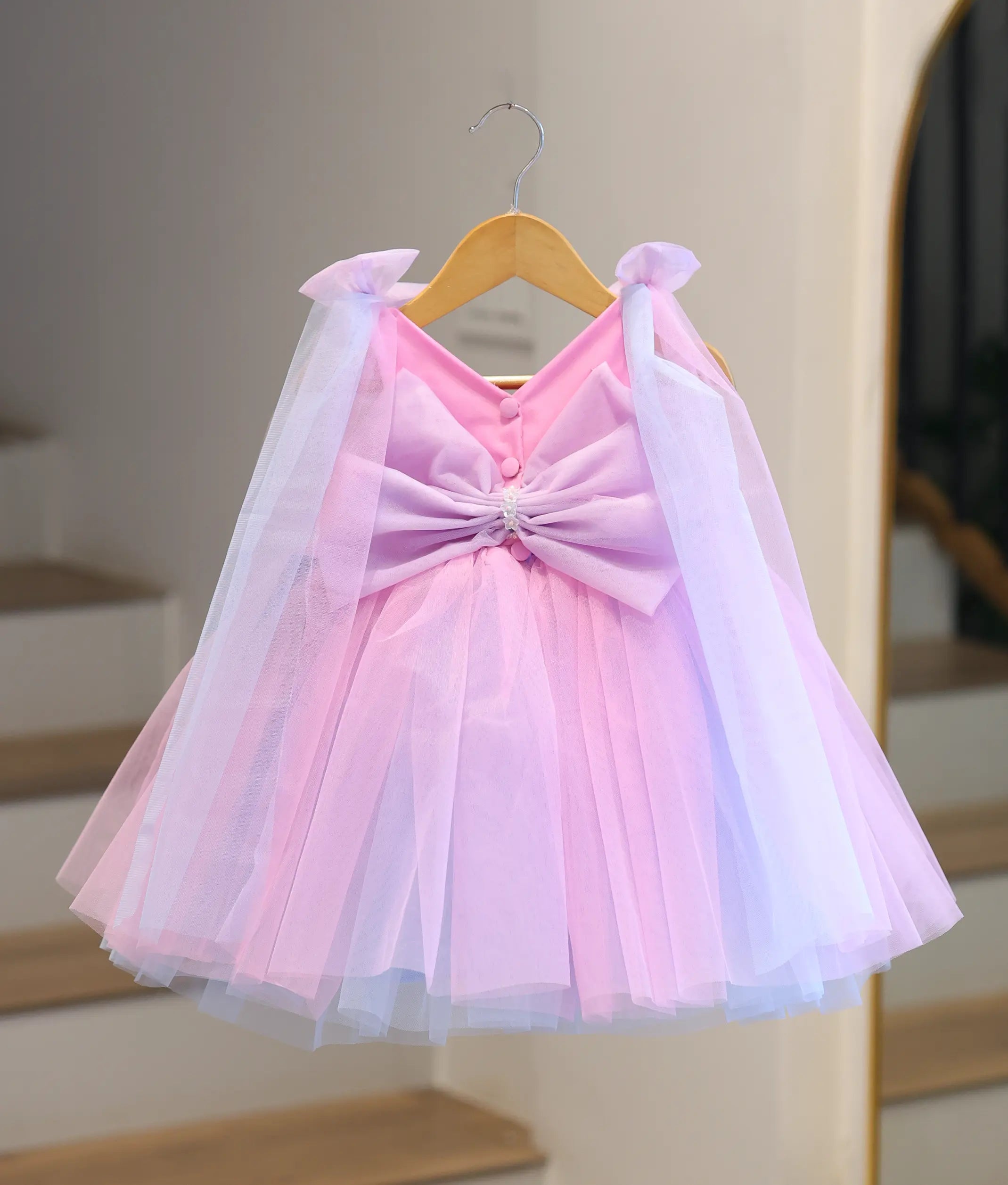 Back view of pink and purple girl's party dress with oversized bow, flowing shoulder drapes and layered princess skirt