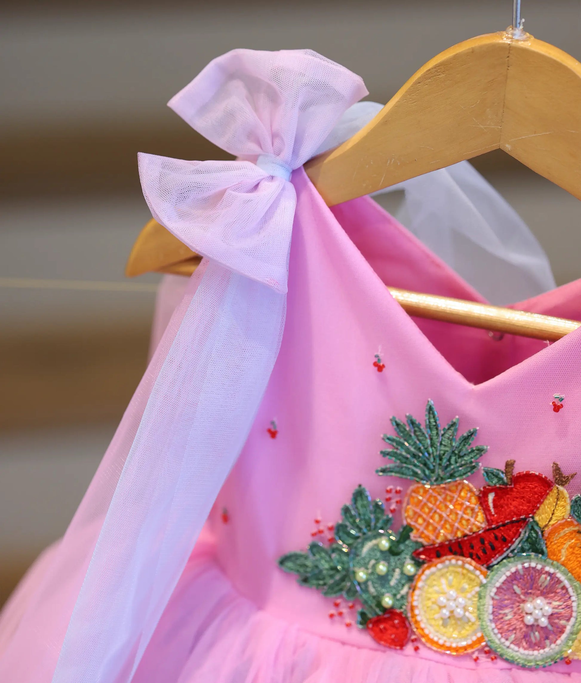 Close-up of girl's party dress with soft shoulder bow, flowing drapes and colorful handcrafted fruit embroidery