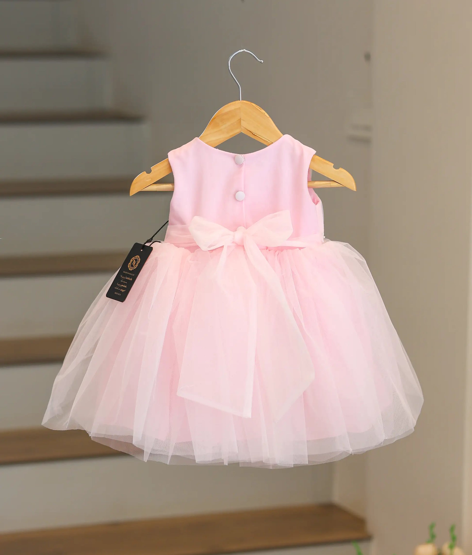 Back view of the pink handworked frock showing the tie bow closure and tulle layers.