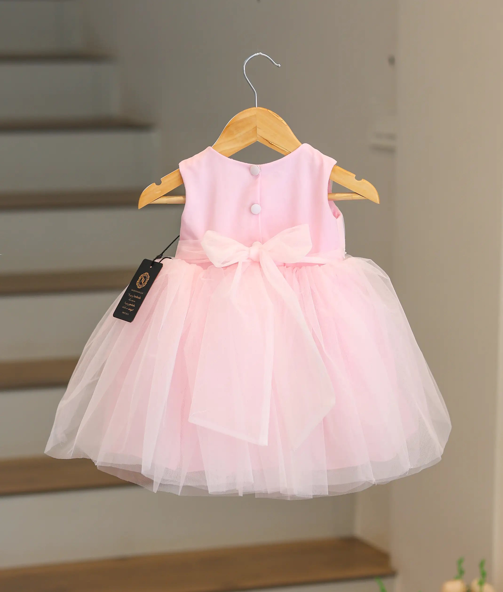 Back view of the pink handworked frock showing the tie bow closure and tulle layers.