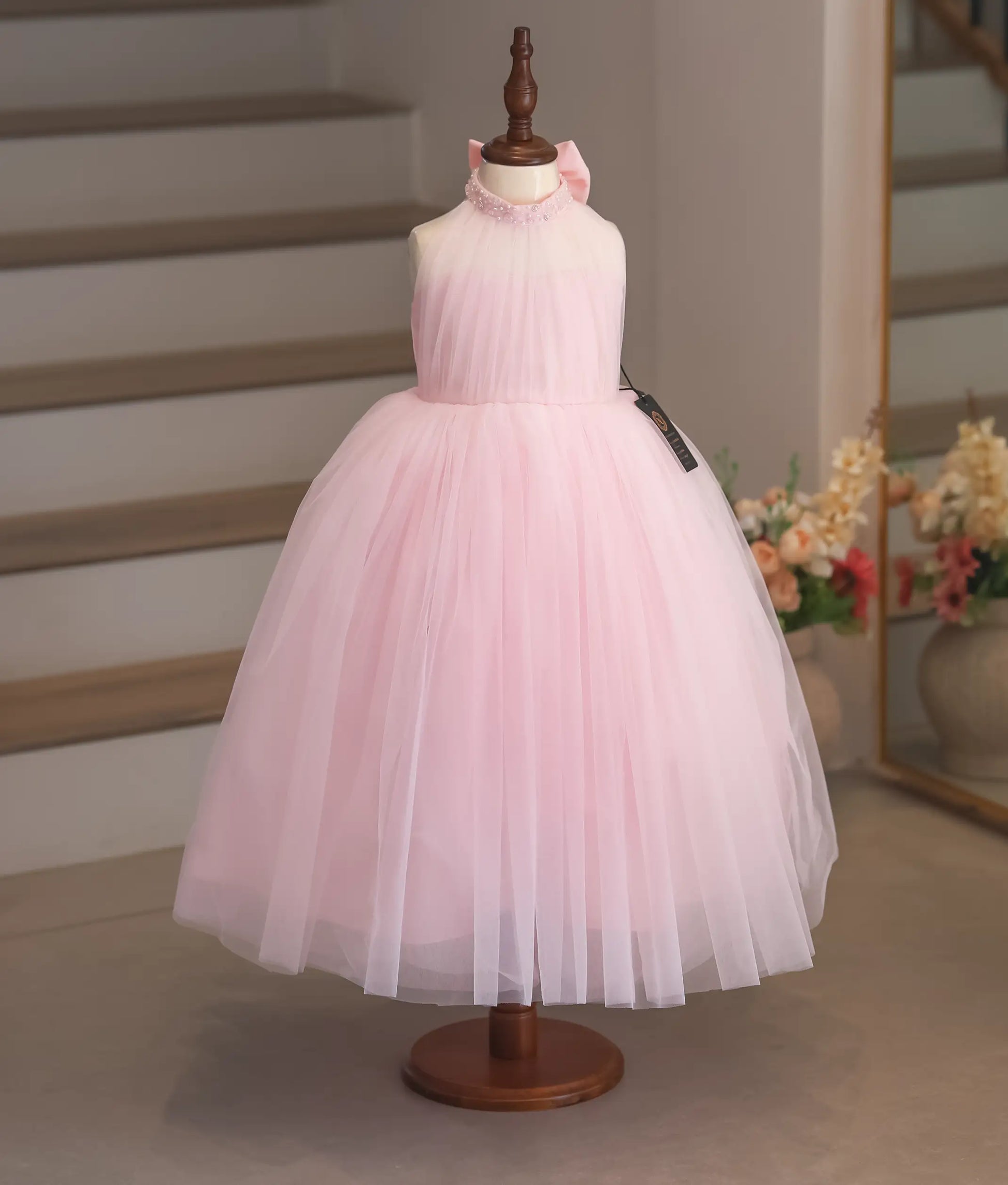 A full-length pink tulle net gown for girls featuring a hand-worked floral neckline and transparent top.