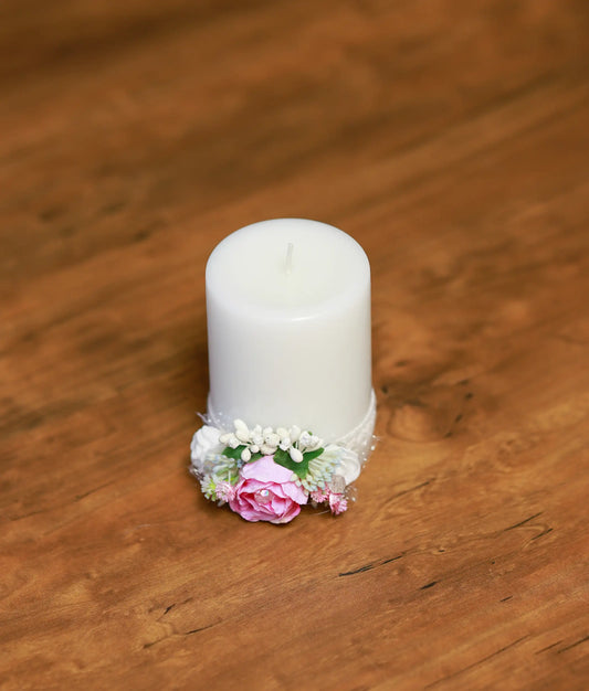 Front view of a white decorative baptism candle with a pink rose, white flowers, and lace detailing