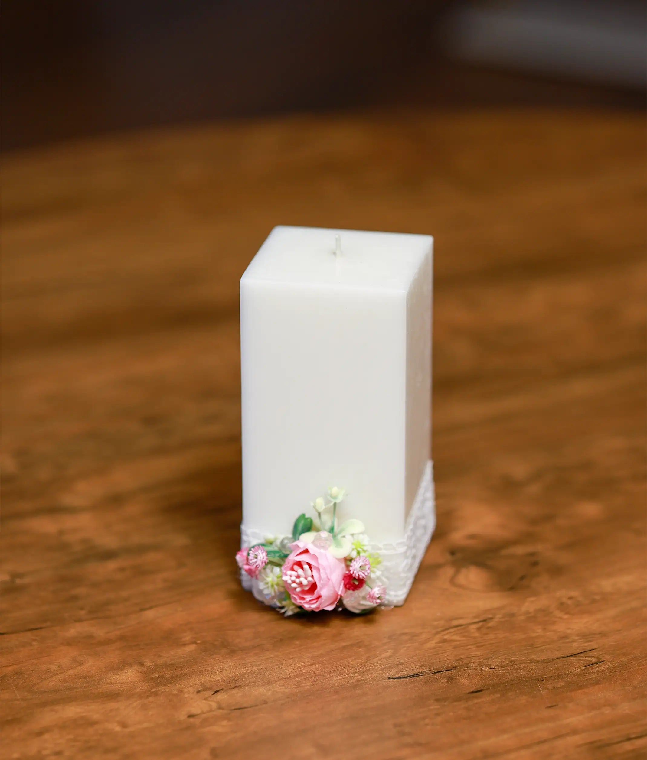 Front view of a white baptism candle decorated with pink and white flowers and a layered satin ribbon