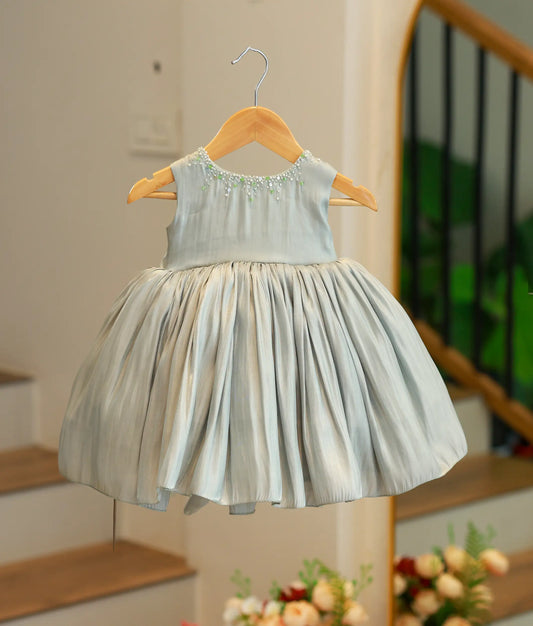 Front view of a green tulle net birthday frock for girls featuring butterfly ruffled sleeves, a pearl-scattered bodice, and a multi-layered skirt with a ruffled hem.
