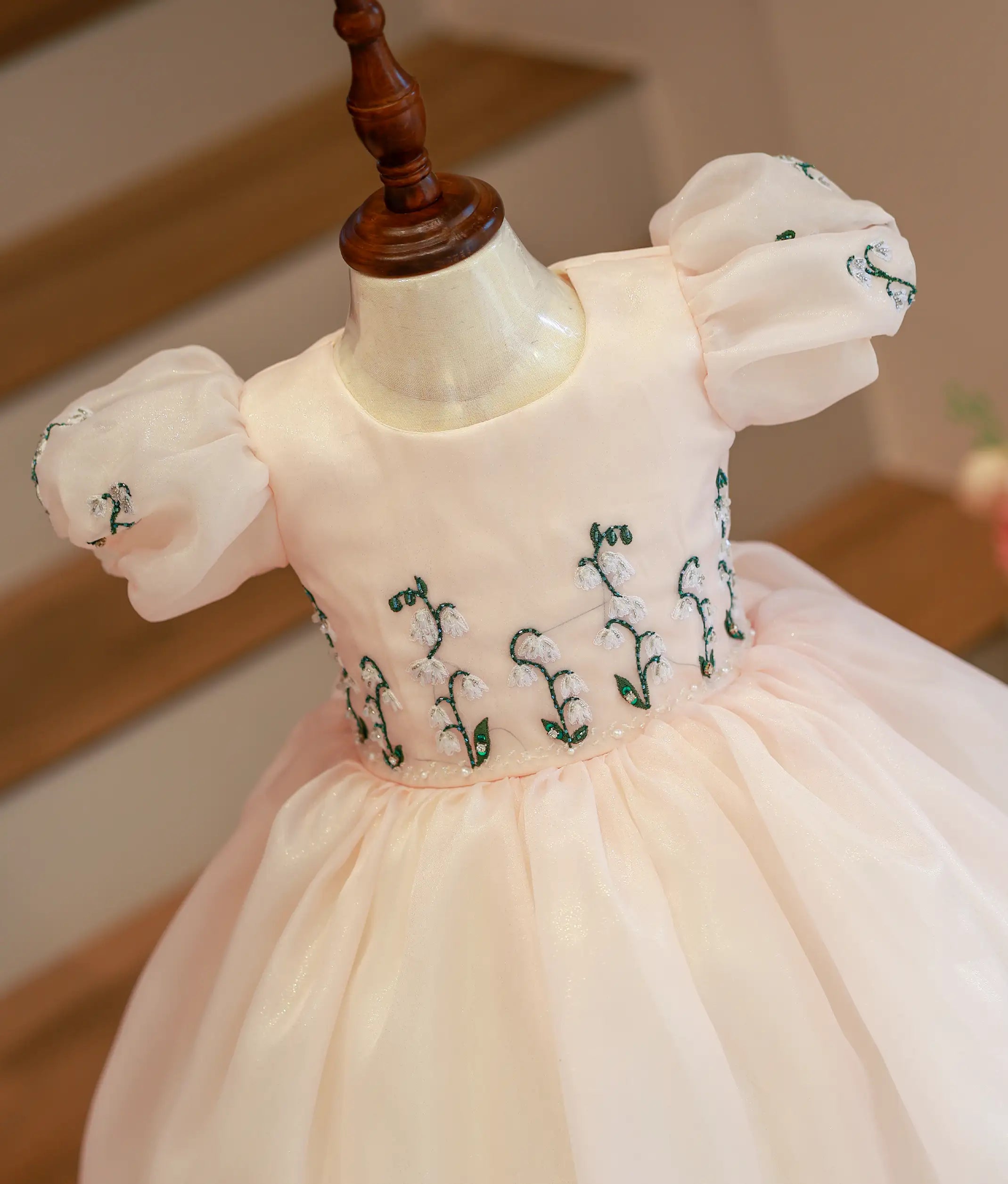 Close-up of the powder peach bodice showing green and white floral embroidery with pearls, crystals, and puff sleeves