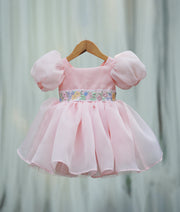 Front view of a powder peach organza girl's birthday frock with puffed sleeves and embroidered waist belt