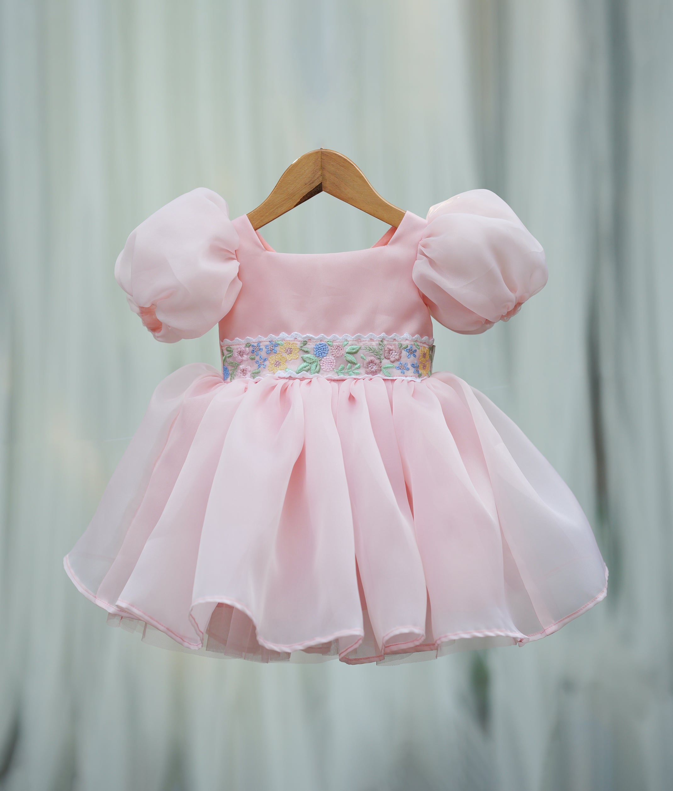 Front view of a powder peach organza girl's birthday frock with puffed sleeves and embroidered waist belt