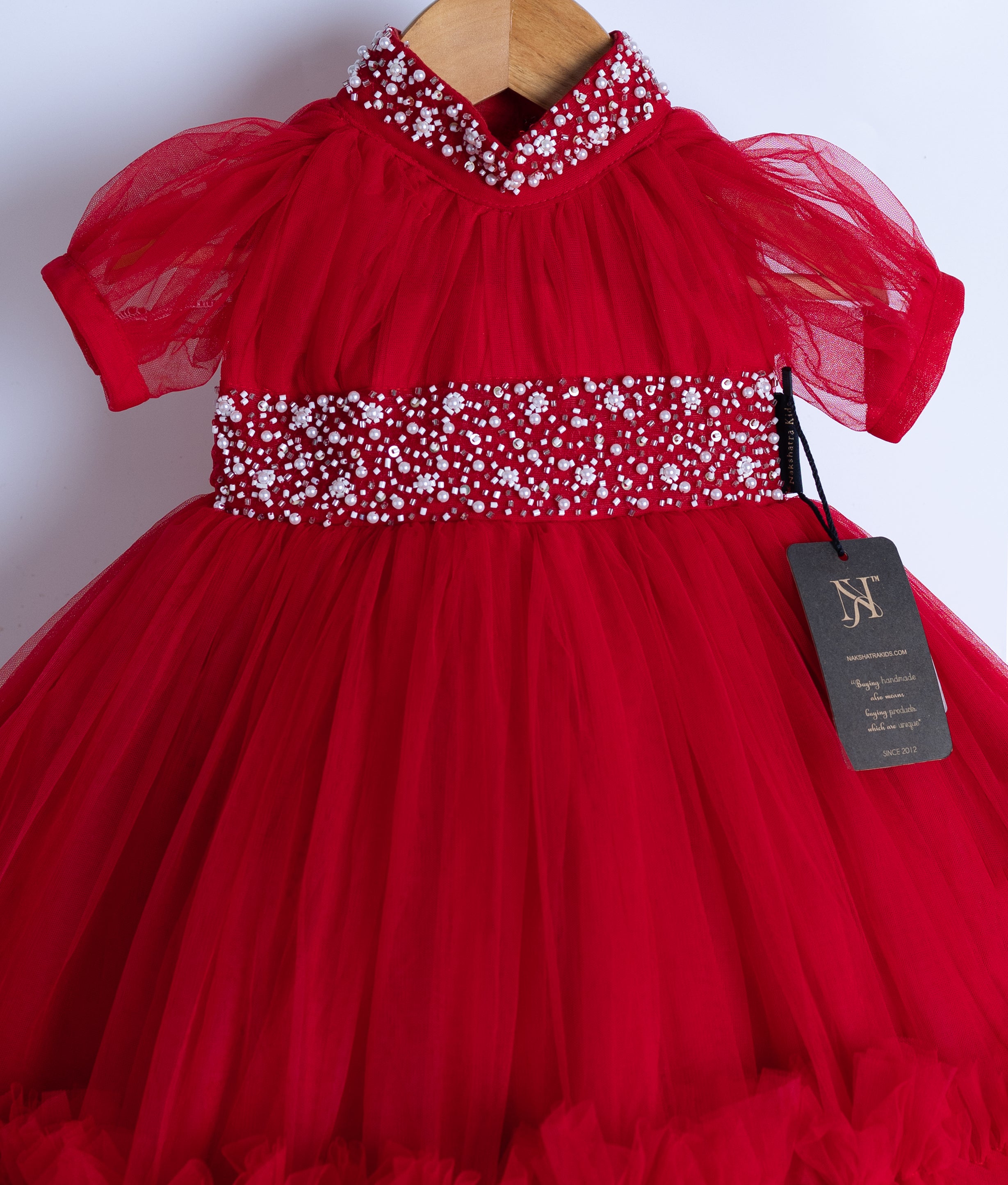 Close-up of red baby dress with puff sleeves and beaded belt on hanger