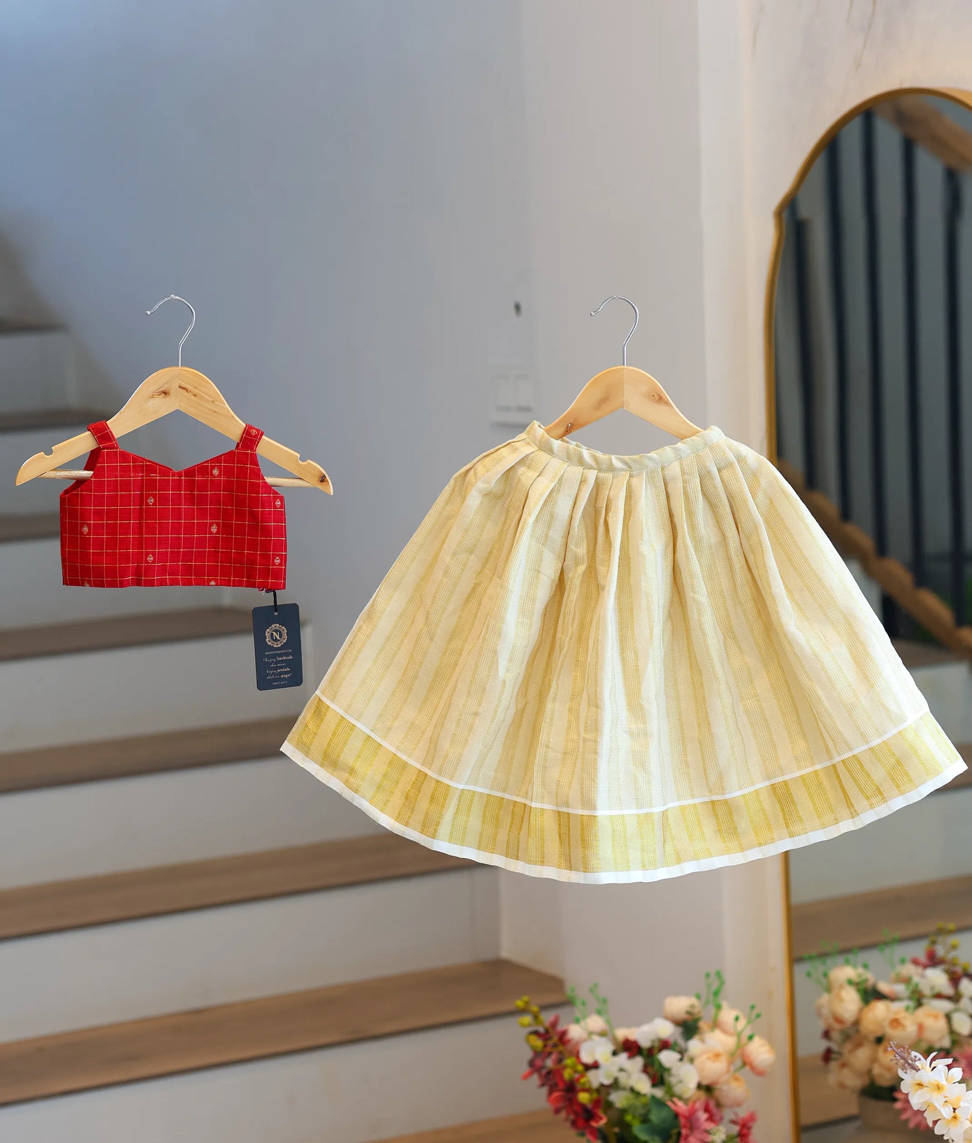 Front view of a girls' red checked top and cream pleated traditional skirt.