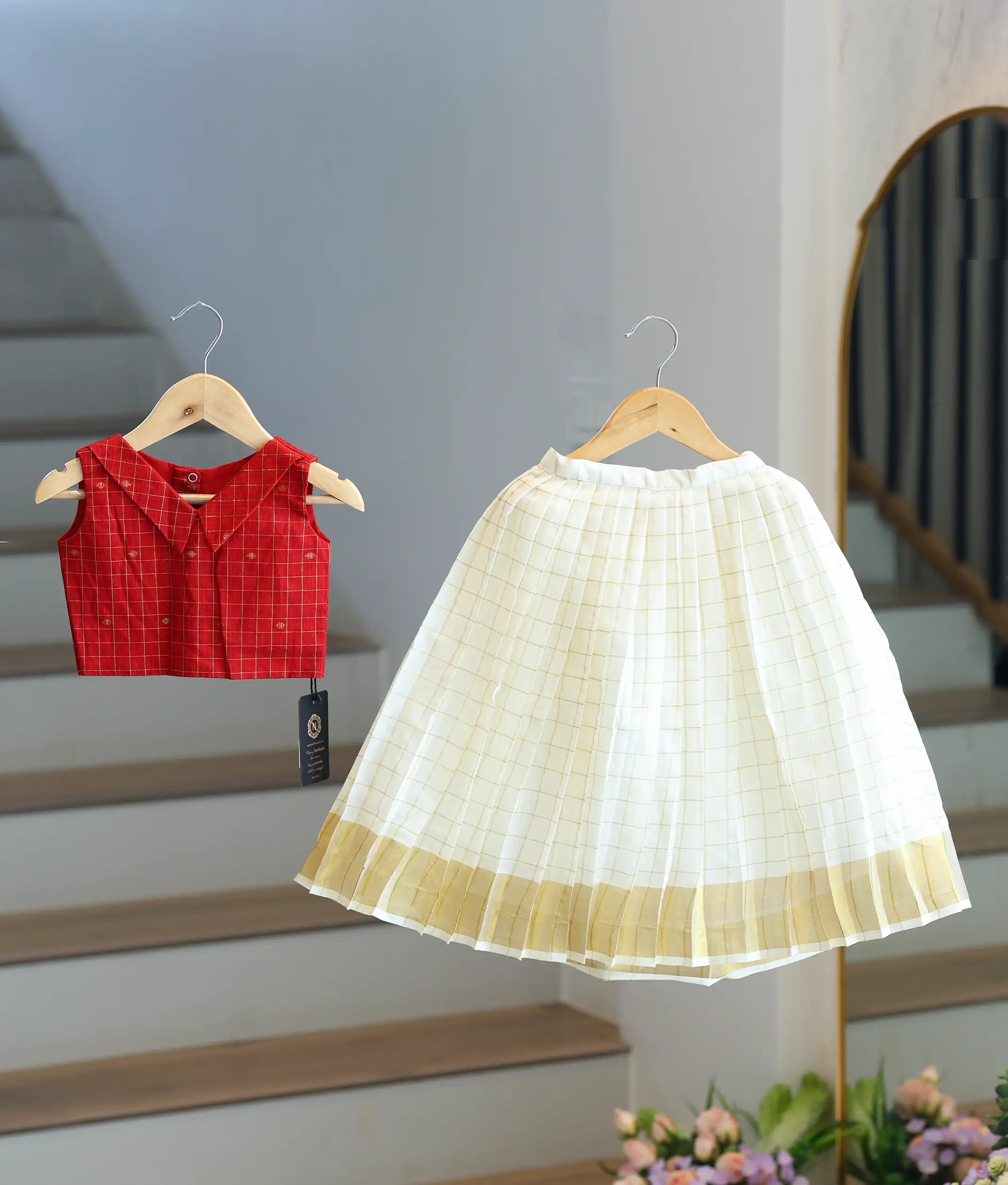 Front view of a girls' red checked top and cream pleated traditional skirt.