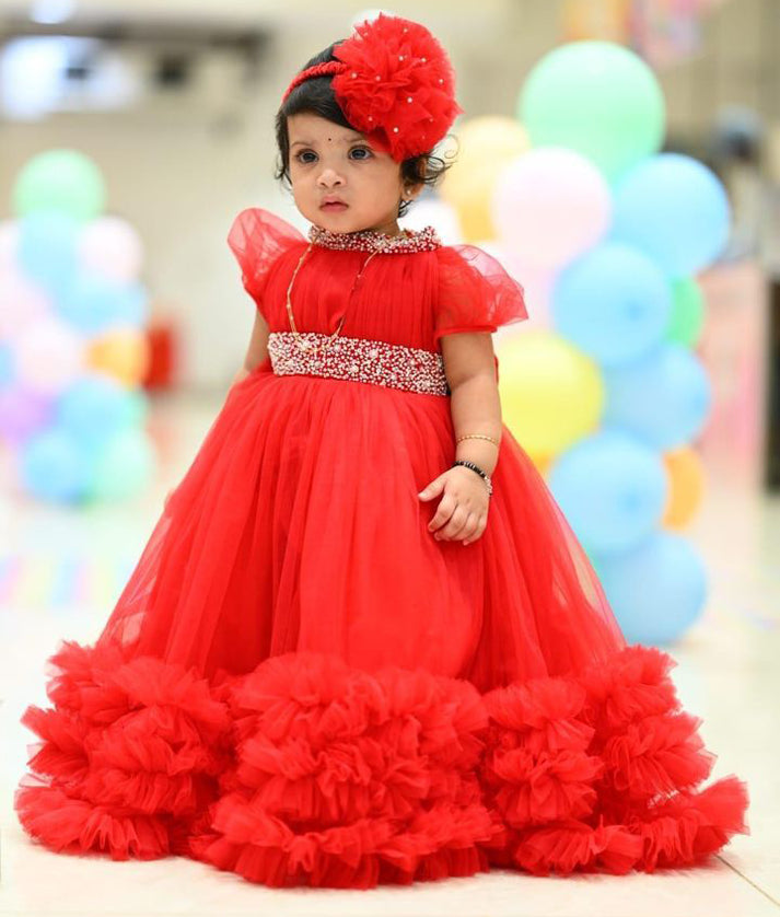 Baby girl wearing red fluffy birthday dress with matching headband and balloons in background