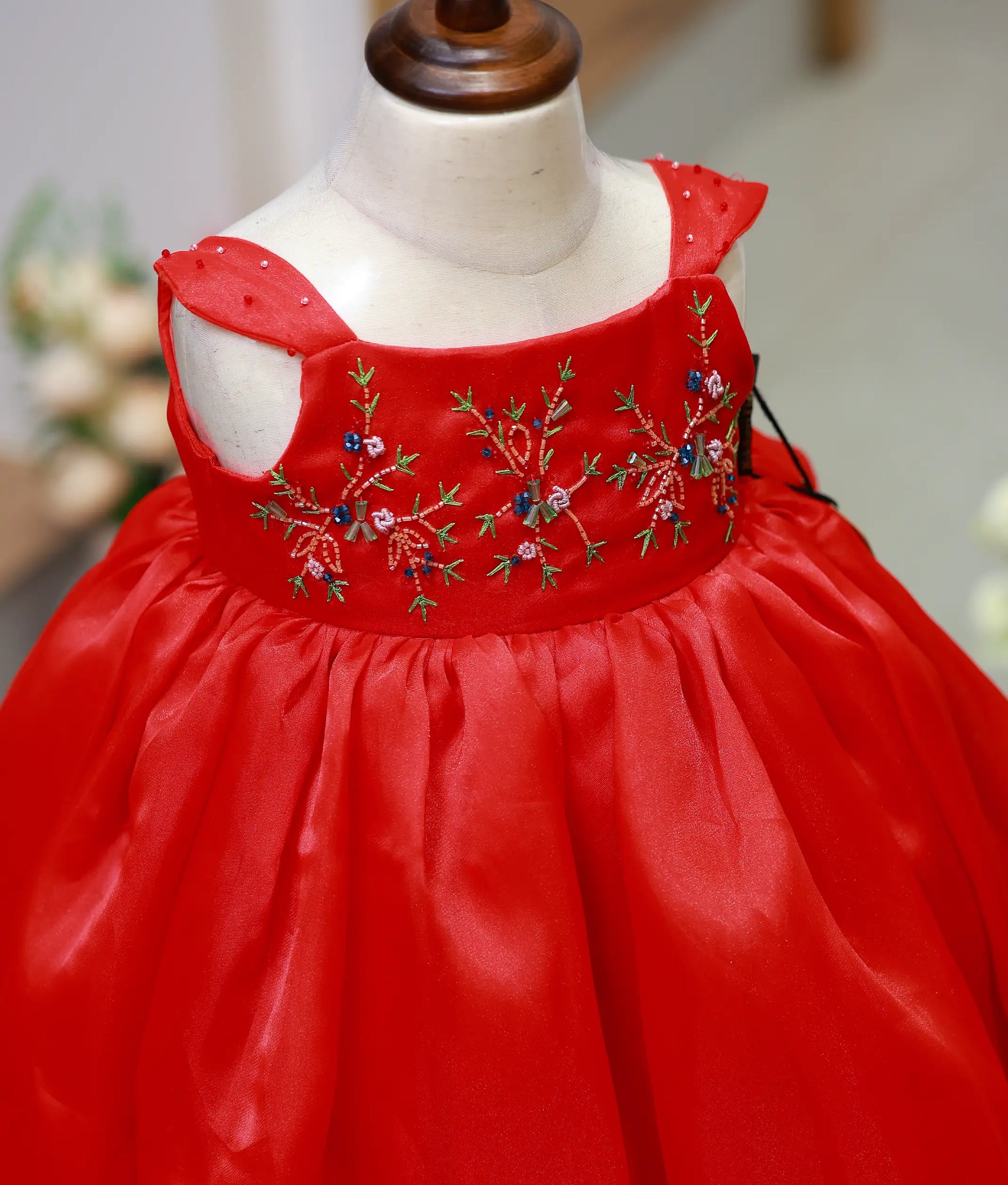 Close-up of the red gown bodice showing the detailed floral hand embroidery and gem-decorated wide straps