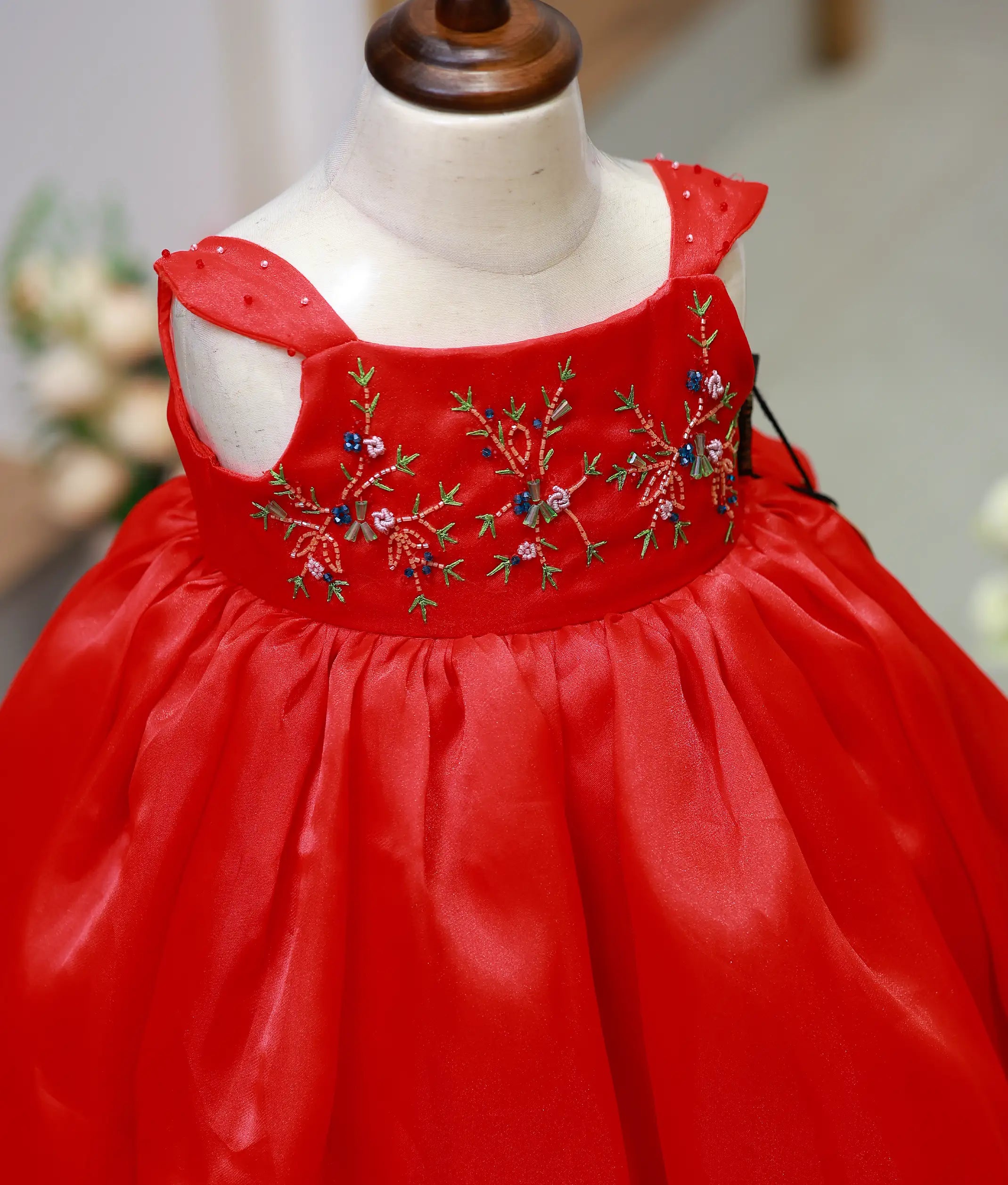 Close-up of the red gown bodice showing the detailed floral hand embroidery and gem-decorated wide straps