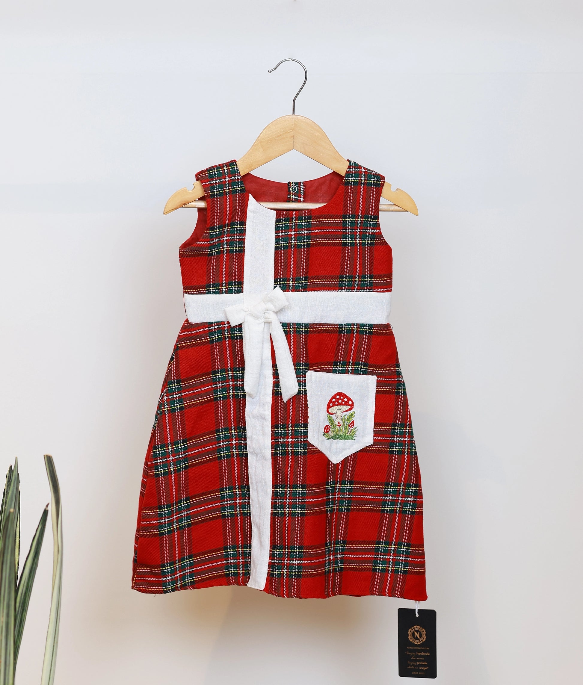 Red and green check cotton Christmas frock for baby girls with a white bow and mushroom pocket detail.