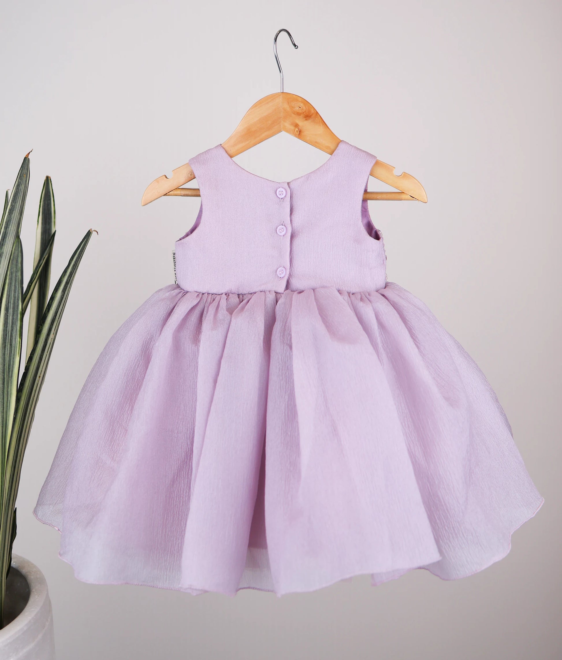 Back view of the pastel lavender crush organza frock featuring a round neckline and a secure button closure