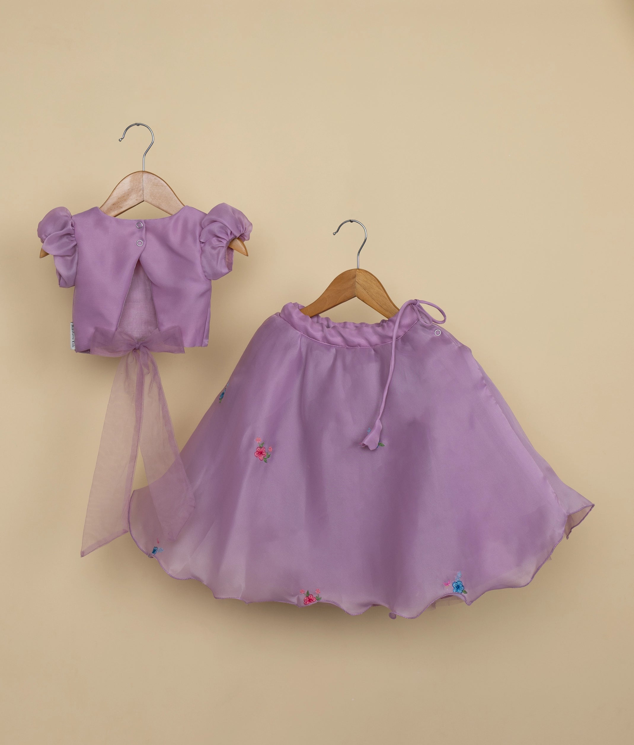 Back view of the pastel lavender crop top and skirt set featuring a round neckline with a button closure and fabric tie