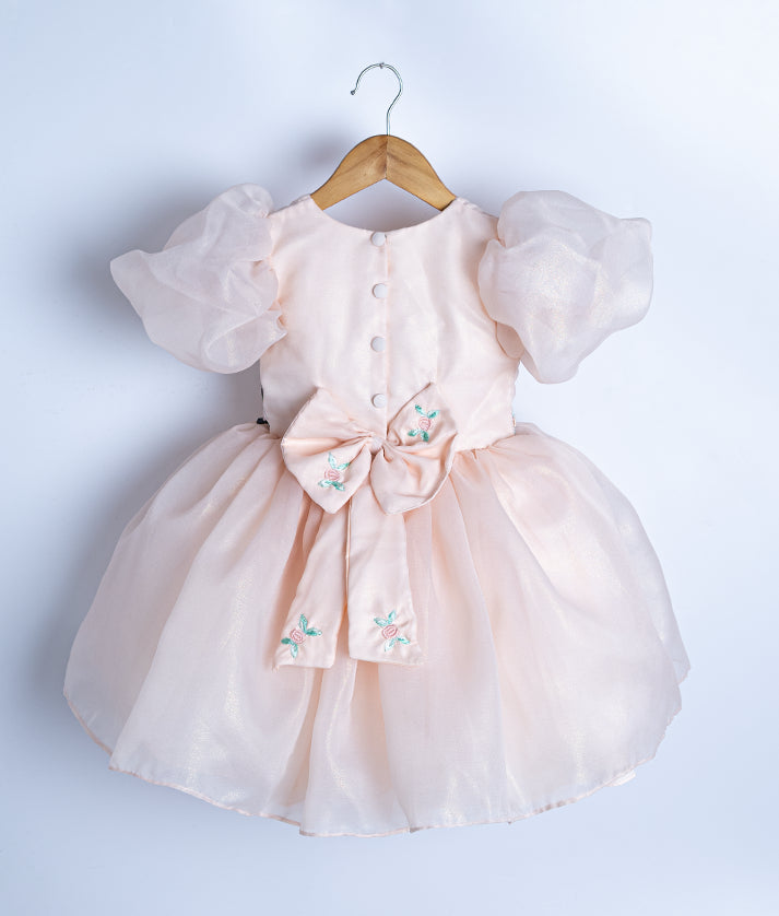 Back view of the pastel peach frock highlighting the round neck, embroidered bow, and tie closure