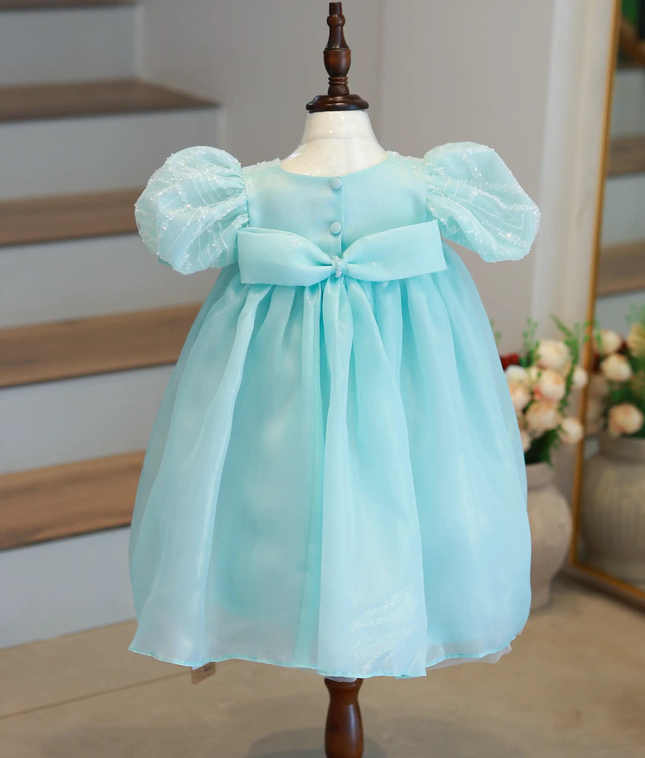 Back view of the powder blue frock featuring a large crystal-embellished bow and show button closure