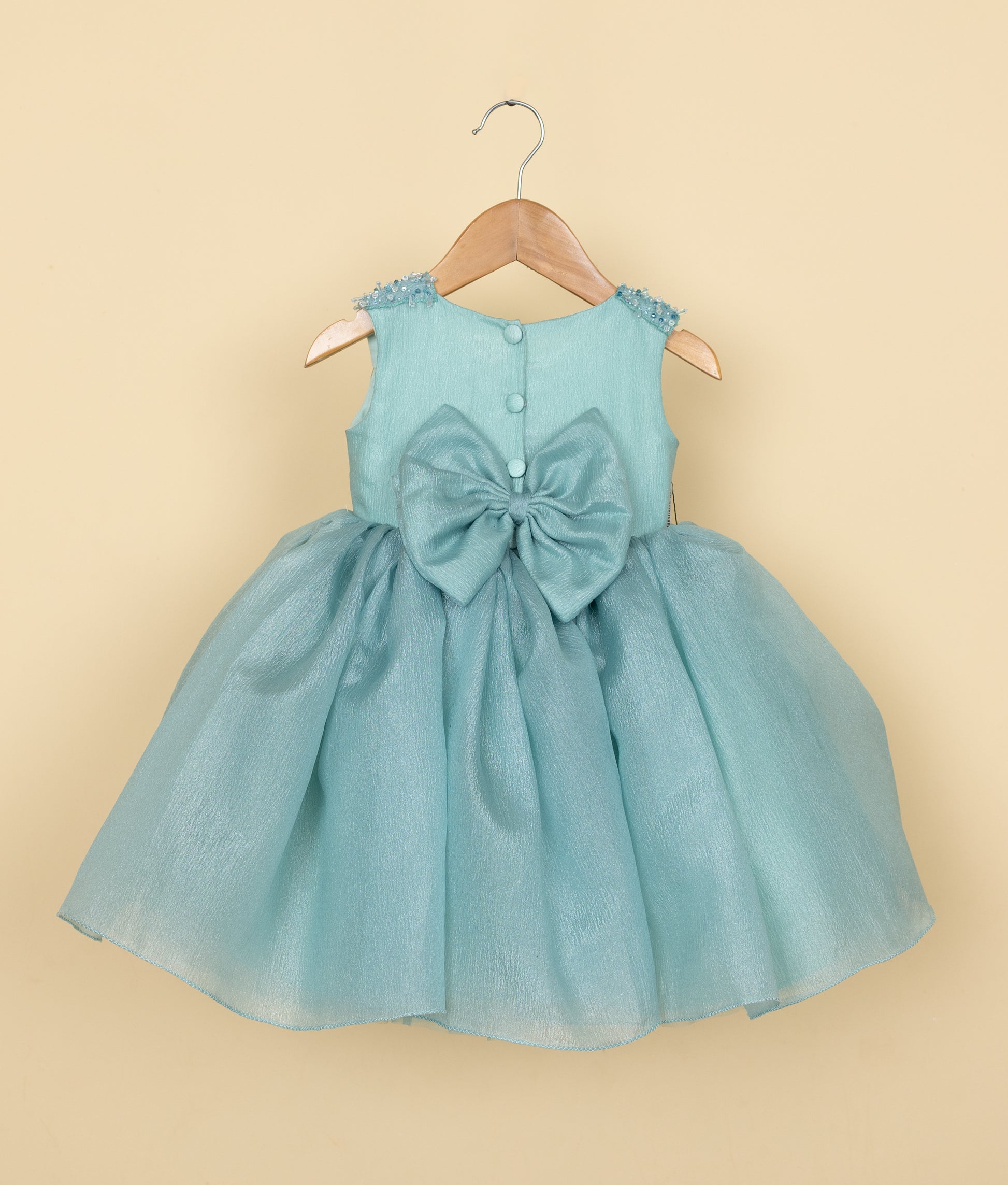 Back view of the Munsell blue organza frock featuring a round neckline, show button, and a decorative bow
