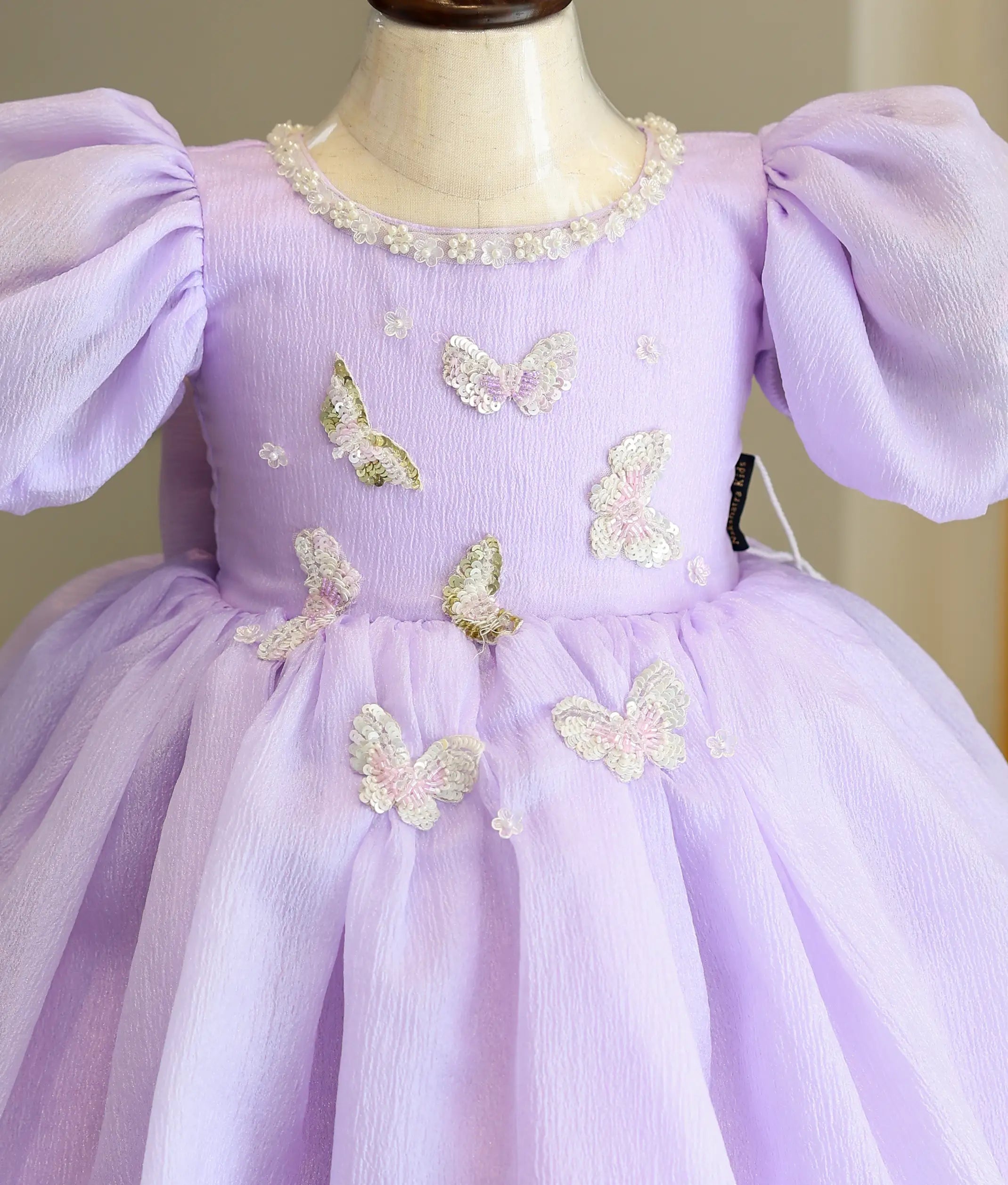 Close-up of the lavender frock bodice showing butterfly appliqués, silver neckline trim, and pearl-trimmed puff sleeves