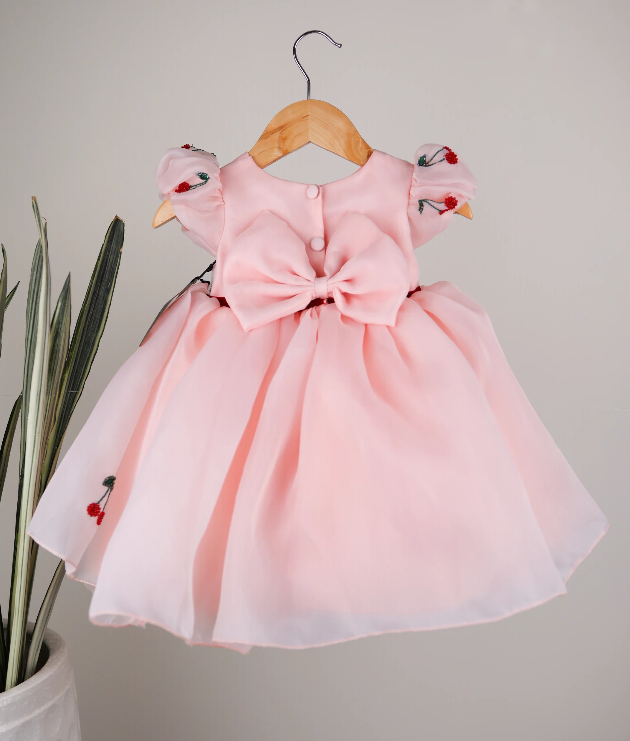 Back view of the pastel peach cherry theme dress featuring a round neckline, show button, and a decorative bow